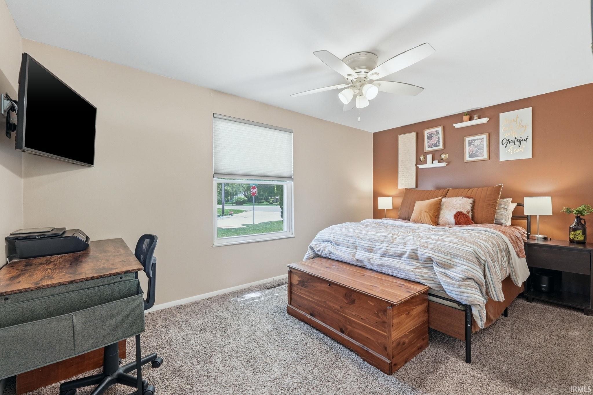 Carpeted room featuring a ceiling fan, a window with blinds, and a built-in wall-mounted television bracket