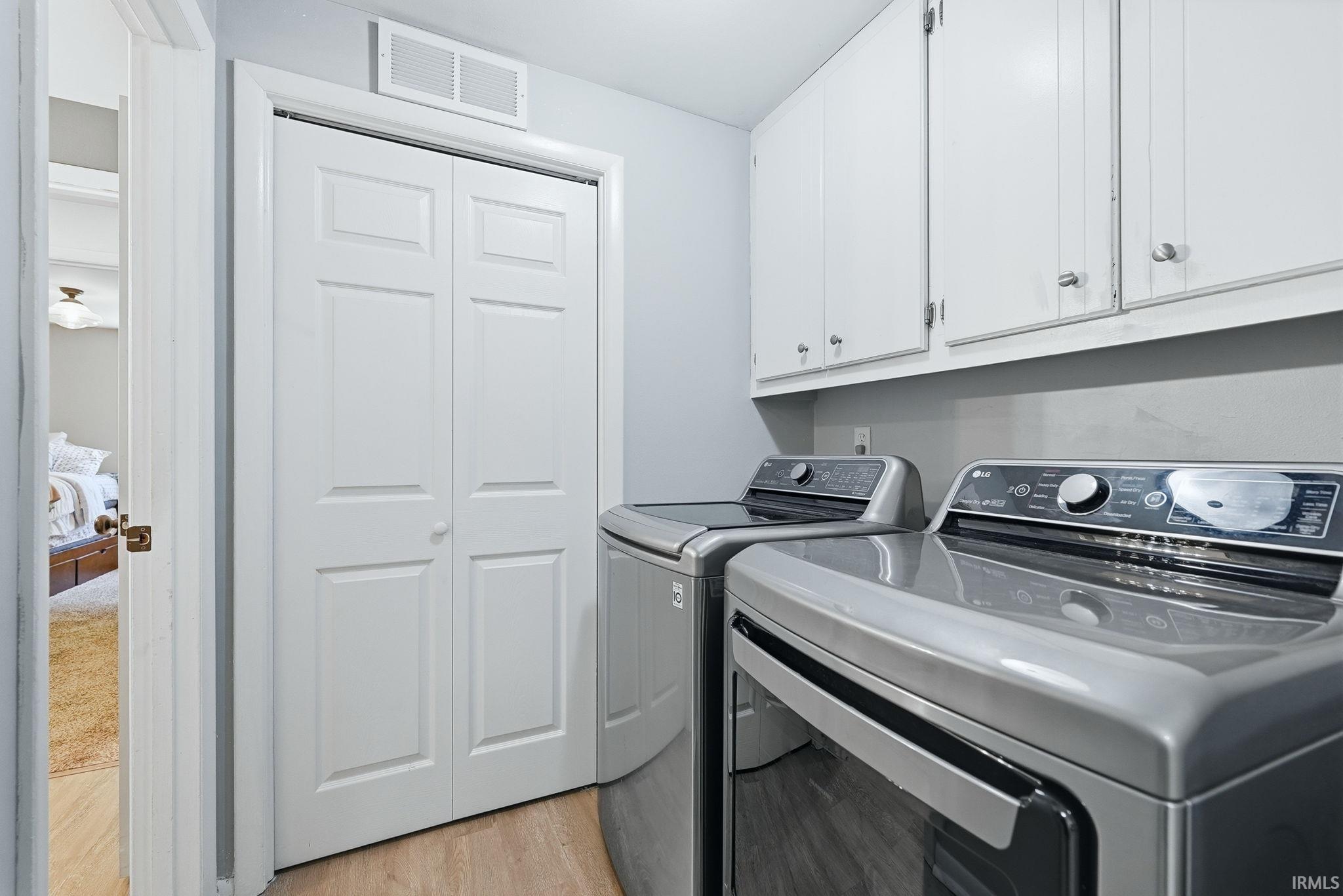 Dedicated laundry area featuring overhead white cabinetry and wood-finish flooring