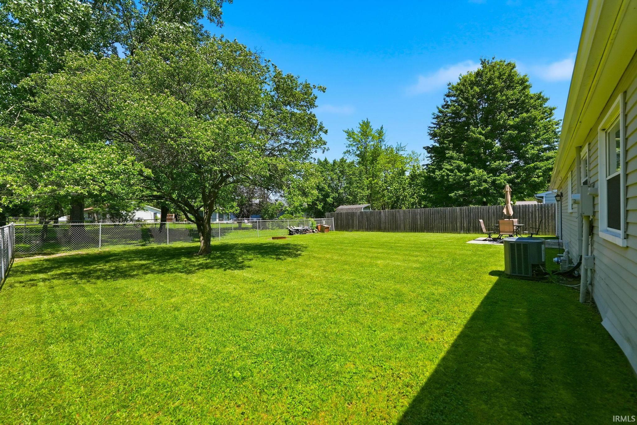 Expansive lawn area featuring a mature shade tree, chain-link fencing, and a privacy fence