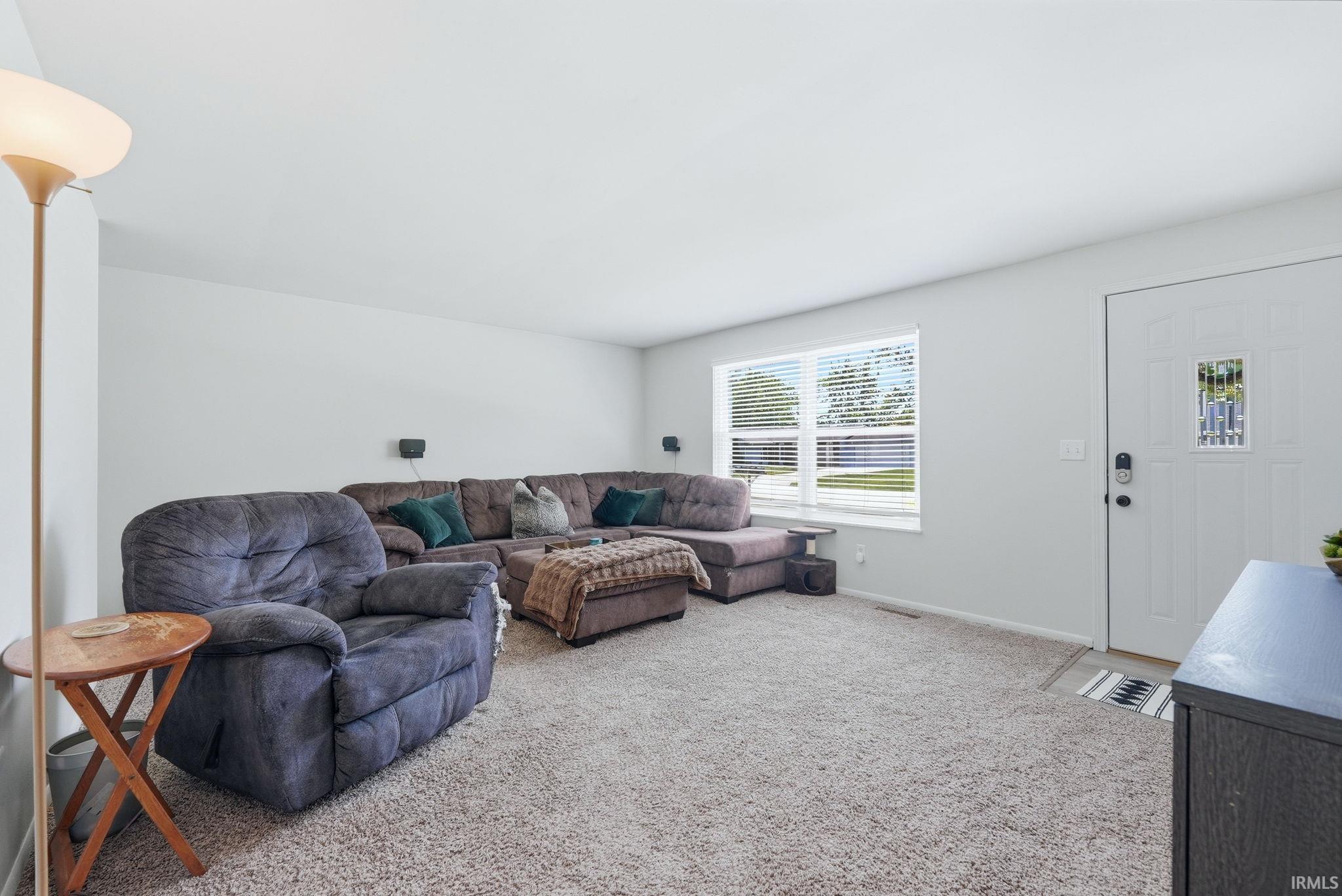 Carpeted living room featuring light-colored walls and a front entry door with a decorative glass insert