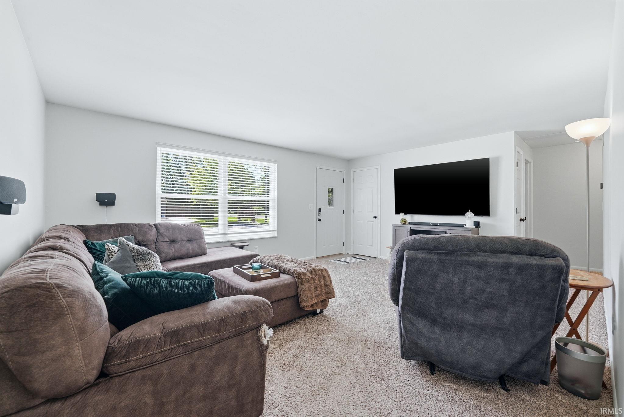 Light-filled living area featuring neutral carpeting, white walls, and a large window with blinds