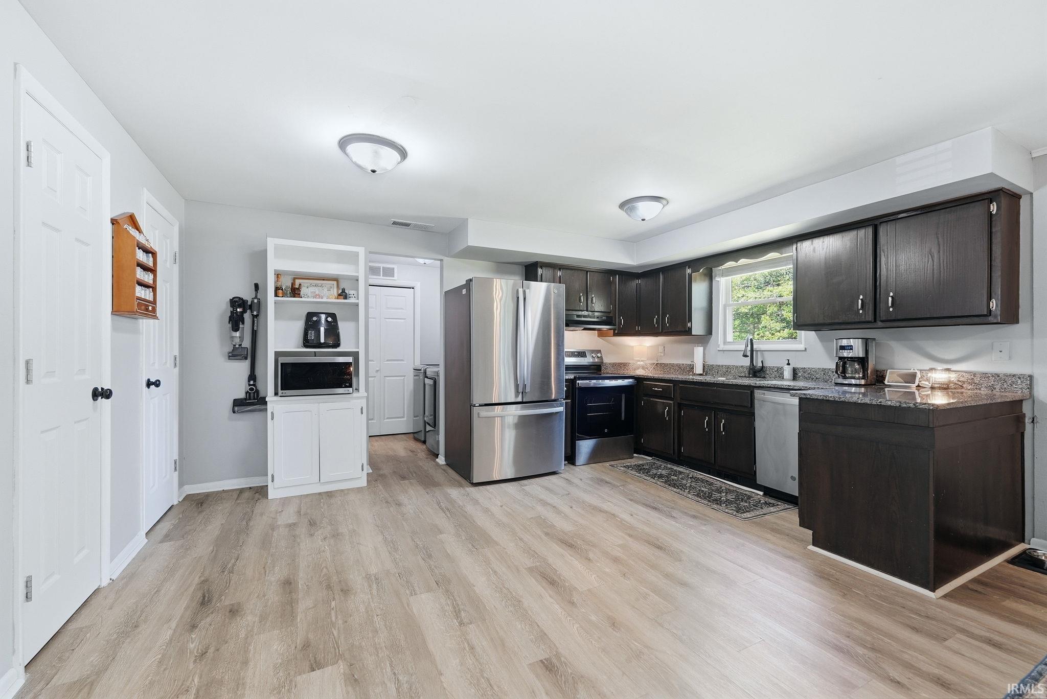 Spacious kitchen featuring wood-finish flooring, dark wood cabinetry, stainless steel appliances, and light-toned countertops