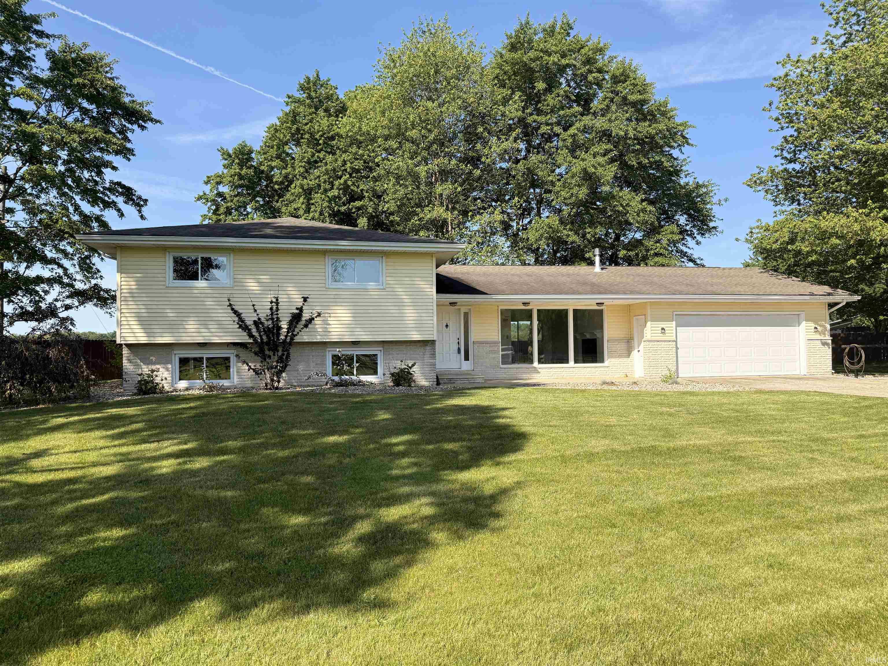 Split-level residence featuring light-colored siding, a dark roofline, and a two-car garage