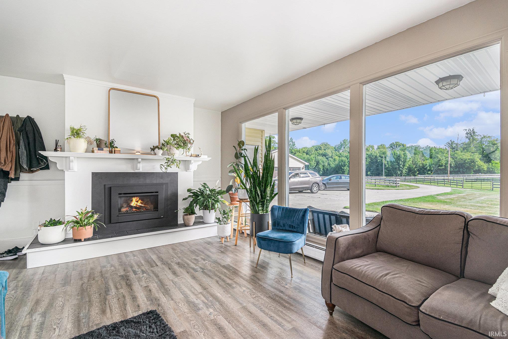 Spacious room featuring wood-finish flooring, a white mantel fireplace with a dark surround, and large picture windows offering abundant natural light