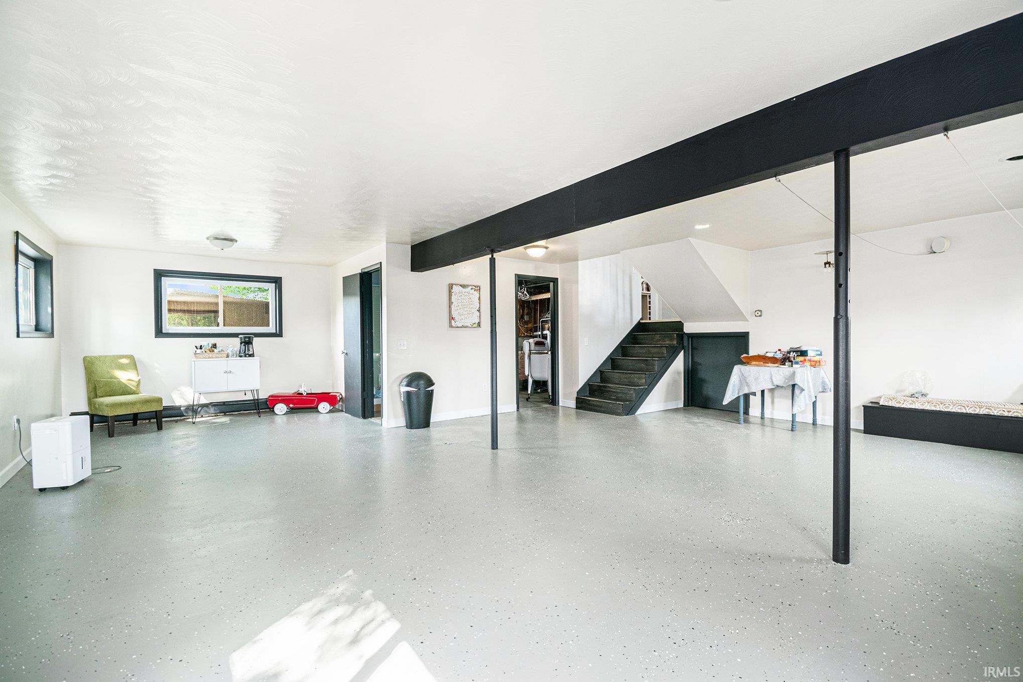 Spacious interior room with light-toned flooring, white walls, and exposed black support beams