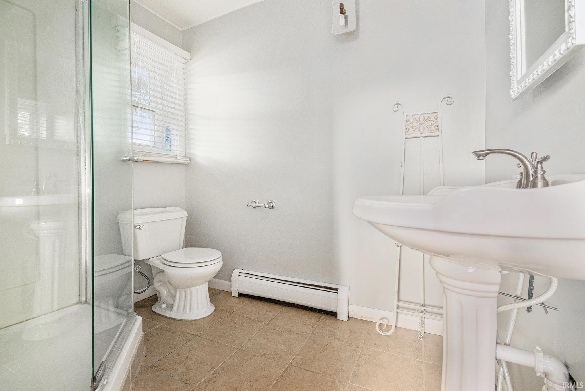 Bathroom featuring a pedestal sink with brushed nickel faucet, glass-enclosed shower, white toilet, and neutral-toned tile flooring