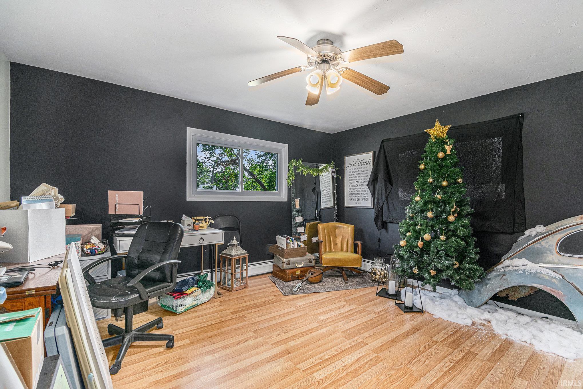 Room featuring wood-finish flooring, a ceiling fan with light fixture, and a white-trimmed window