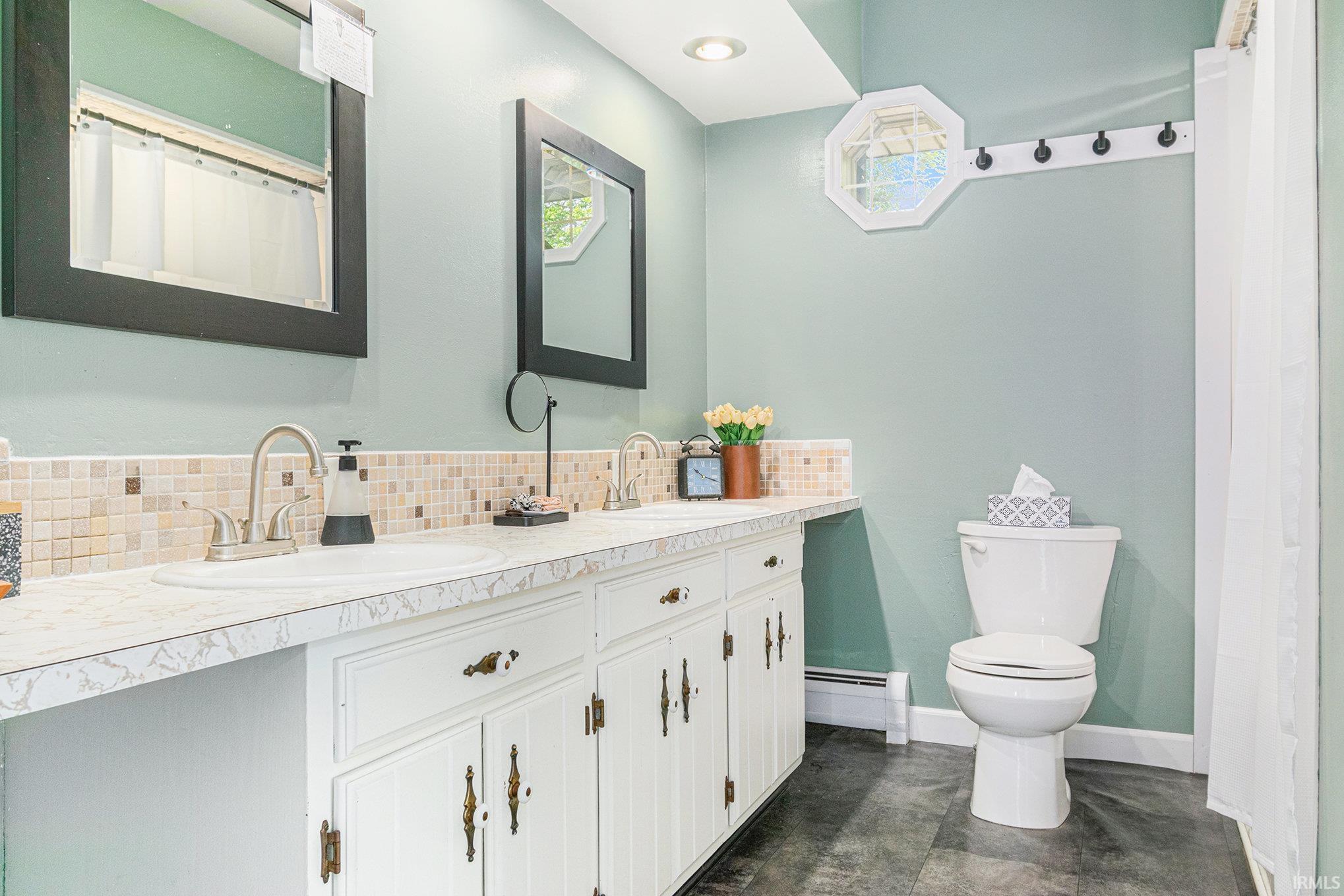 Bathroom featuring a dual vanity with white cabinetry, mosaic tile backsplash, and a decorative octagonal window