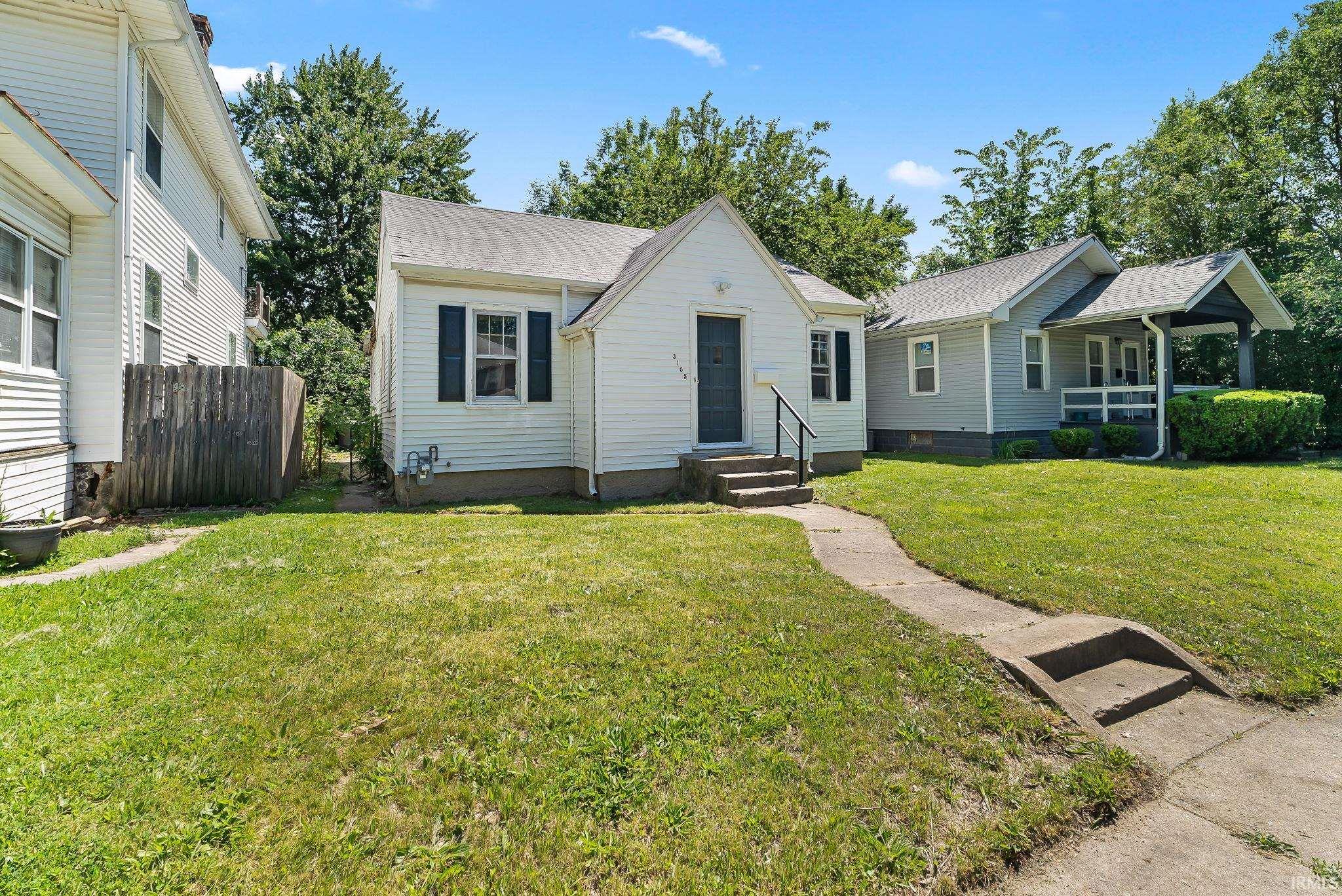 White siding bungalow with a dark entry door and steps featuring black handrails