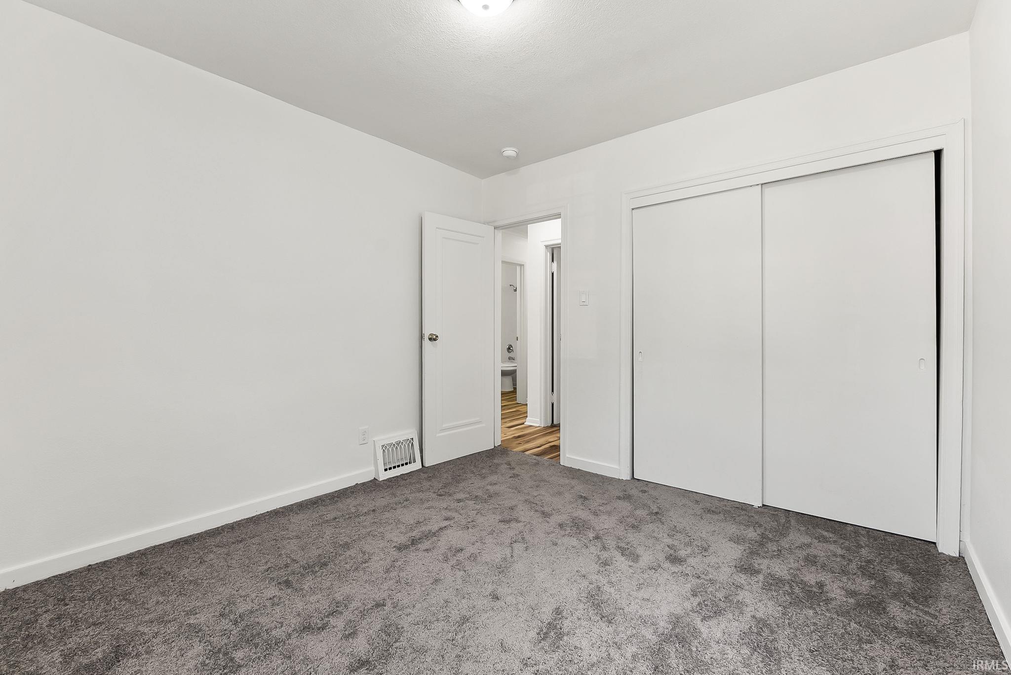 Spacious room featuring gray carpet, white walls, white baseboards, and a double-door closet with sliding panels