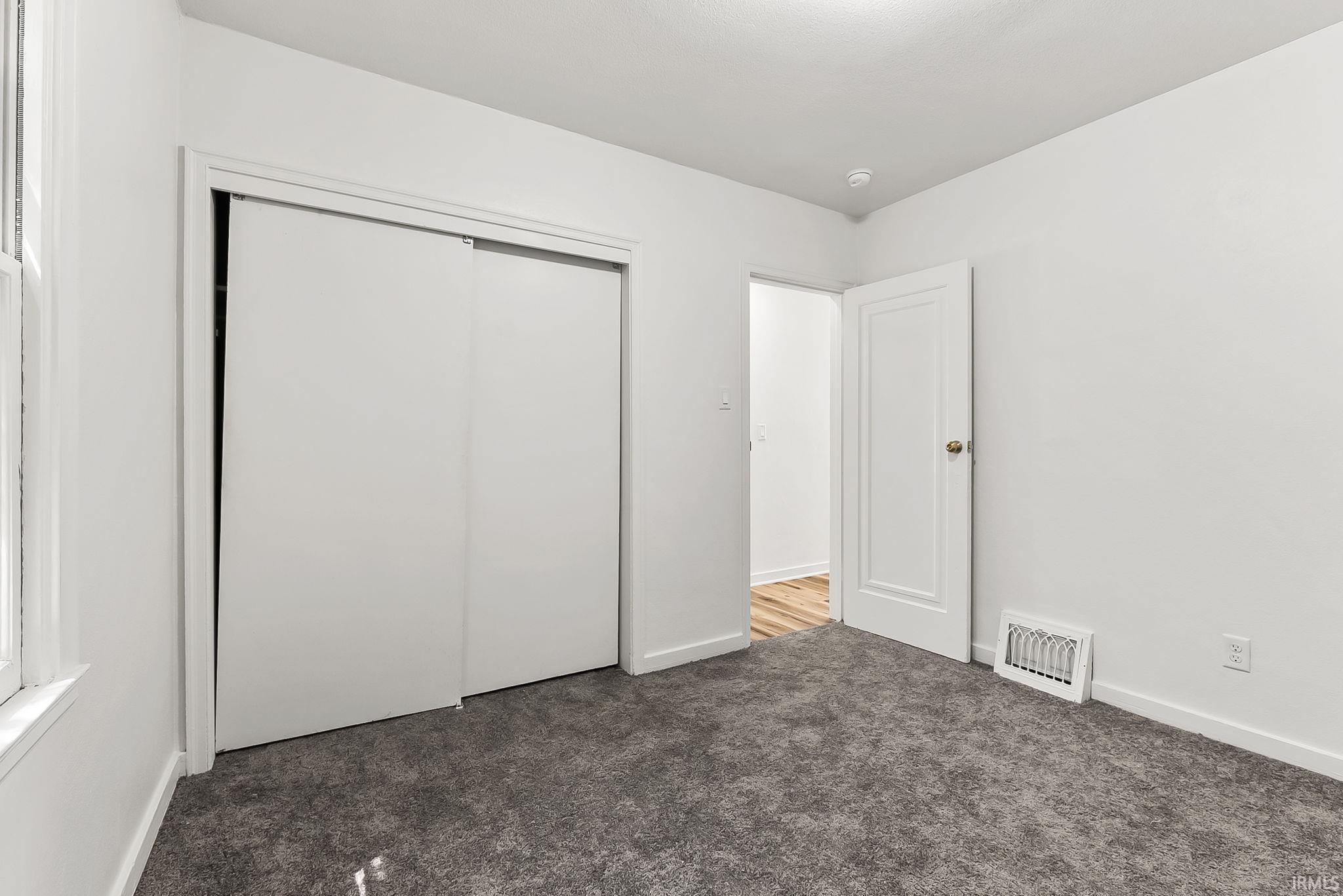 Neutral white walls with gray carpeting, featuring a window with white trim, a double sliding closet, and a white interior door