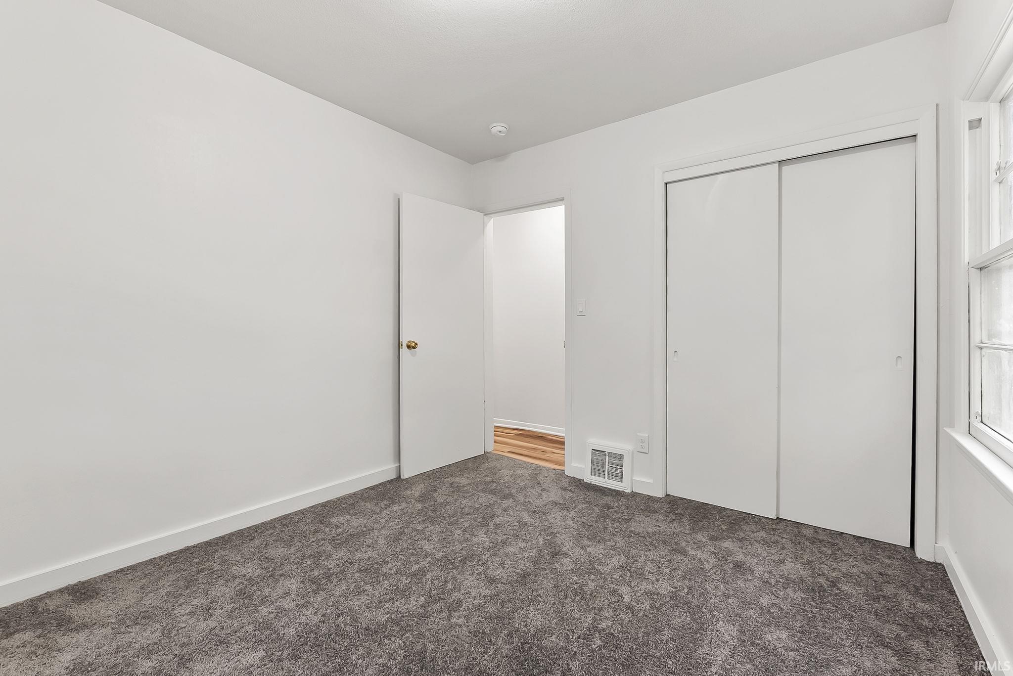 Carpeted room featuring white walls, a closet with sliding doors, a window with muntins, and a doorway opening to wood-finish flooring