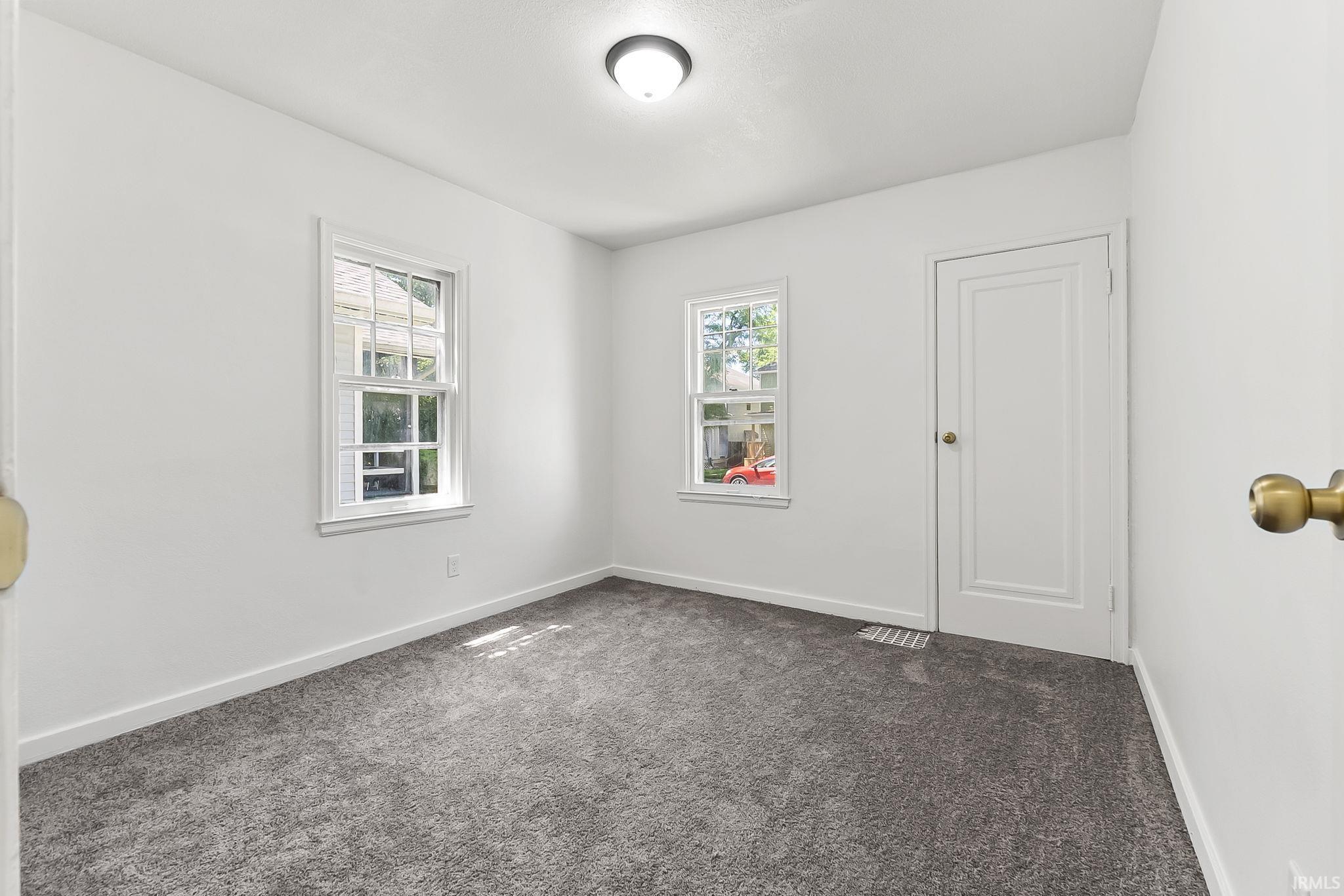 Bedroom featuring two sash windows, light gray carpeting, white trim, a ceiling-mounted light fixture, and a paneled interior door