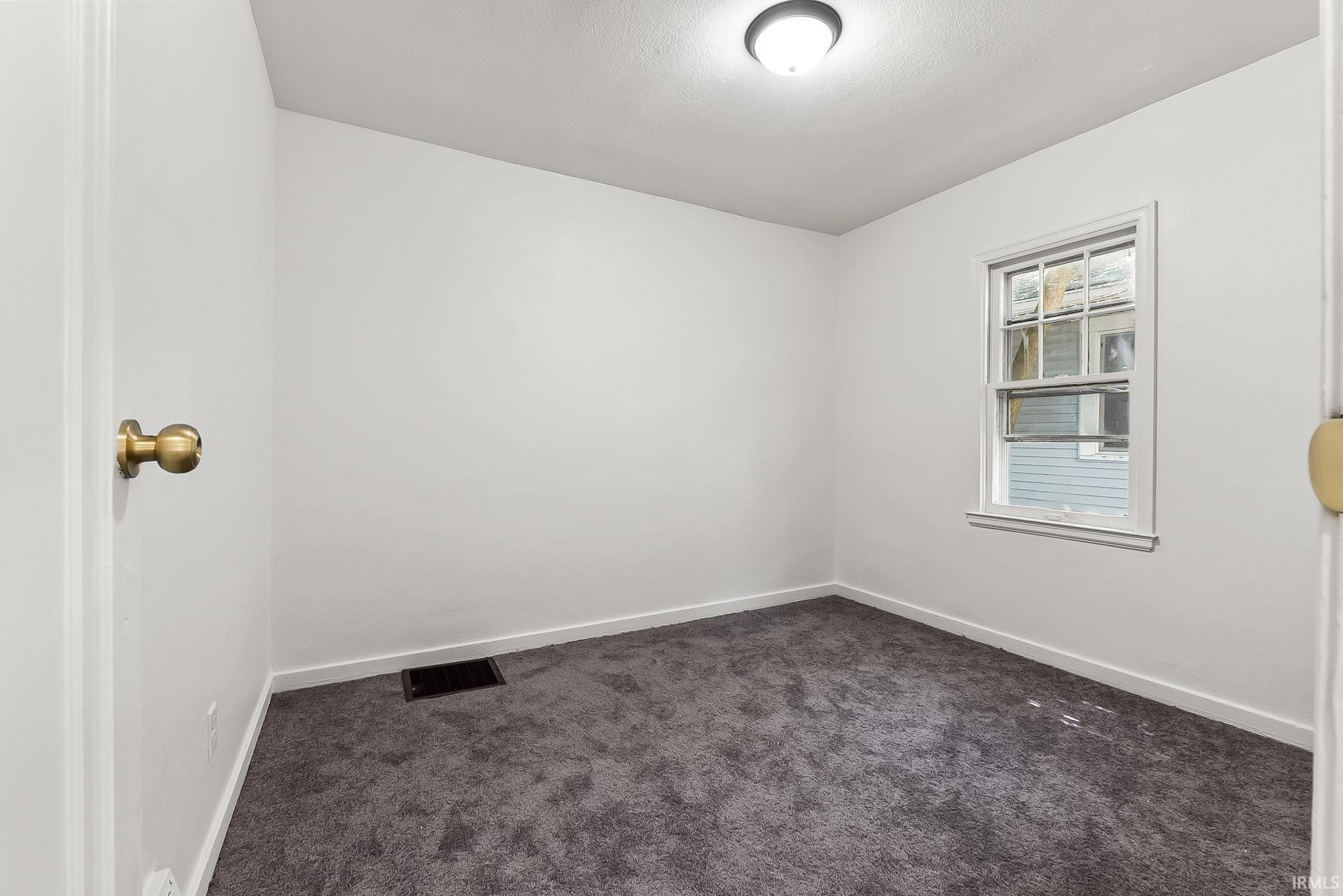Room featuring neutral-toned walls, dark gray carpeting, and a single window with white trim