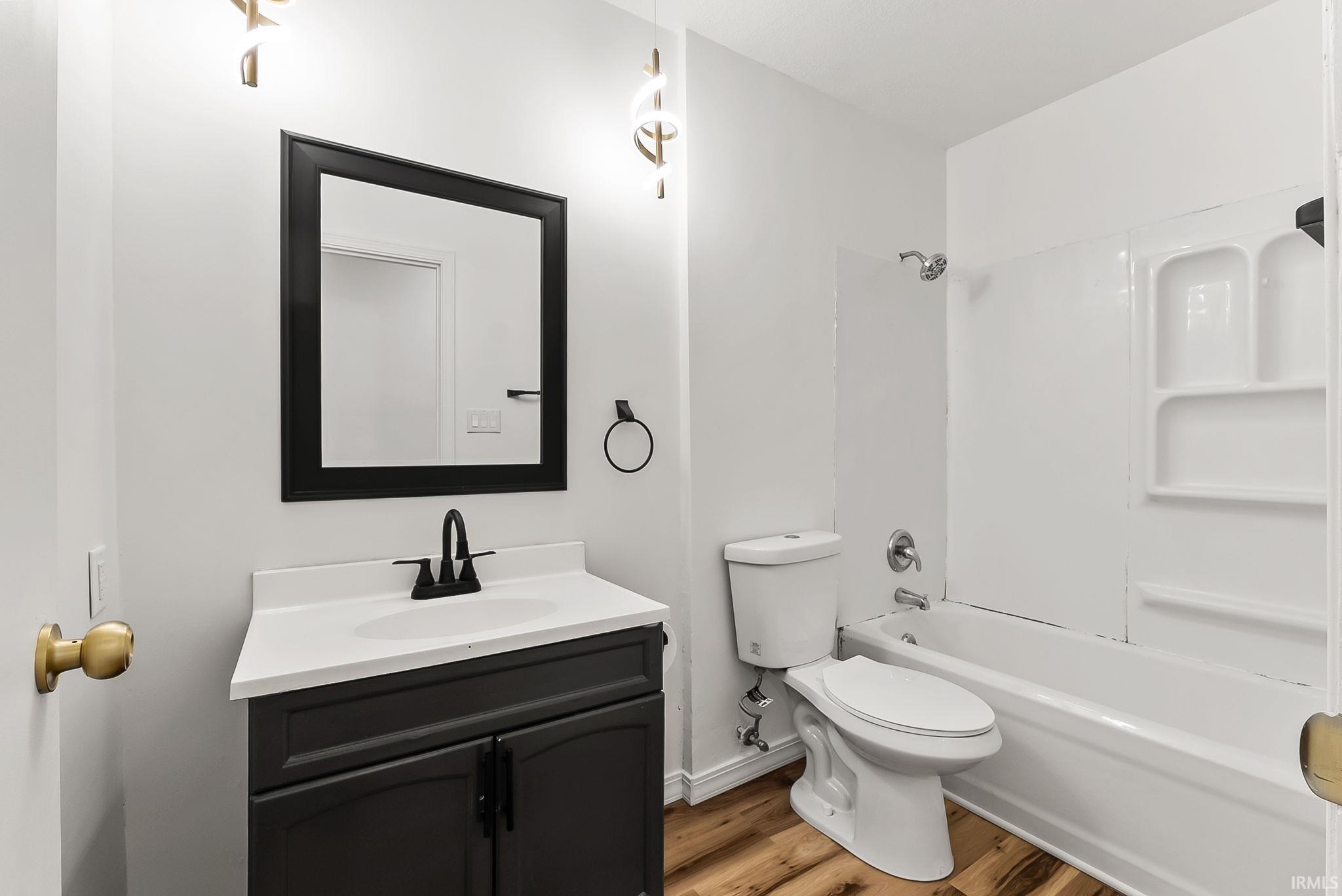 Bathroom with wood-finish flooring, a dark vanity with a white countertop, and a black-framed mirror