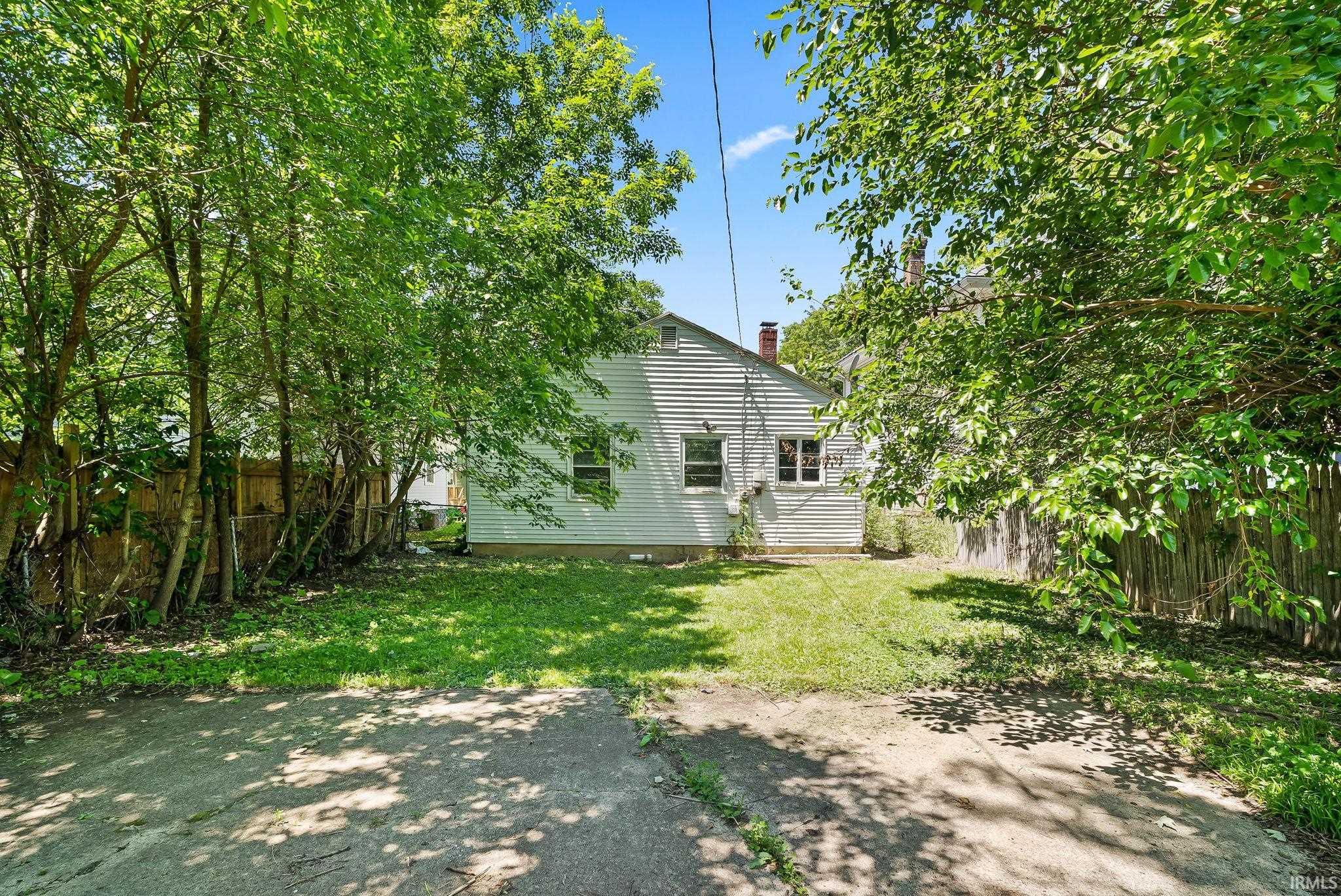 Fenced backyard featuring mature perimeter trees, a grass lawn, and a paved surface