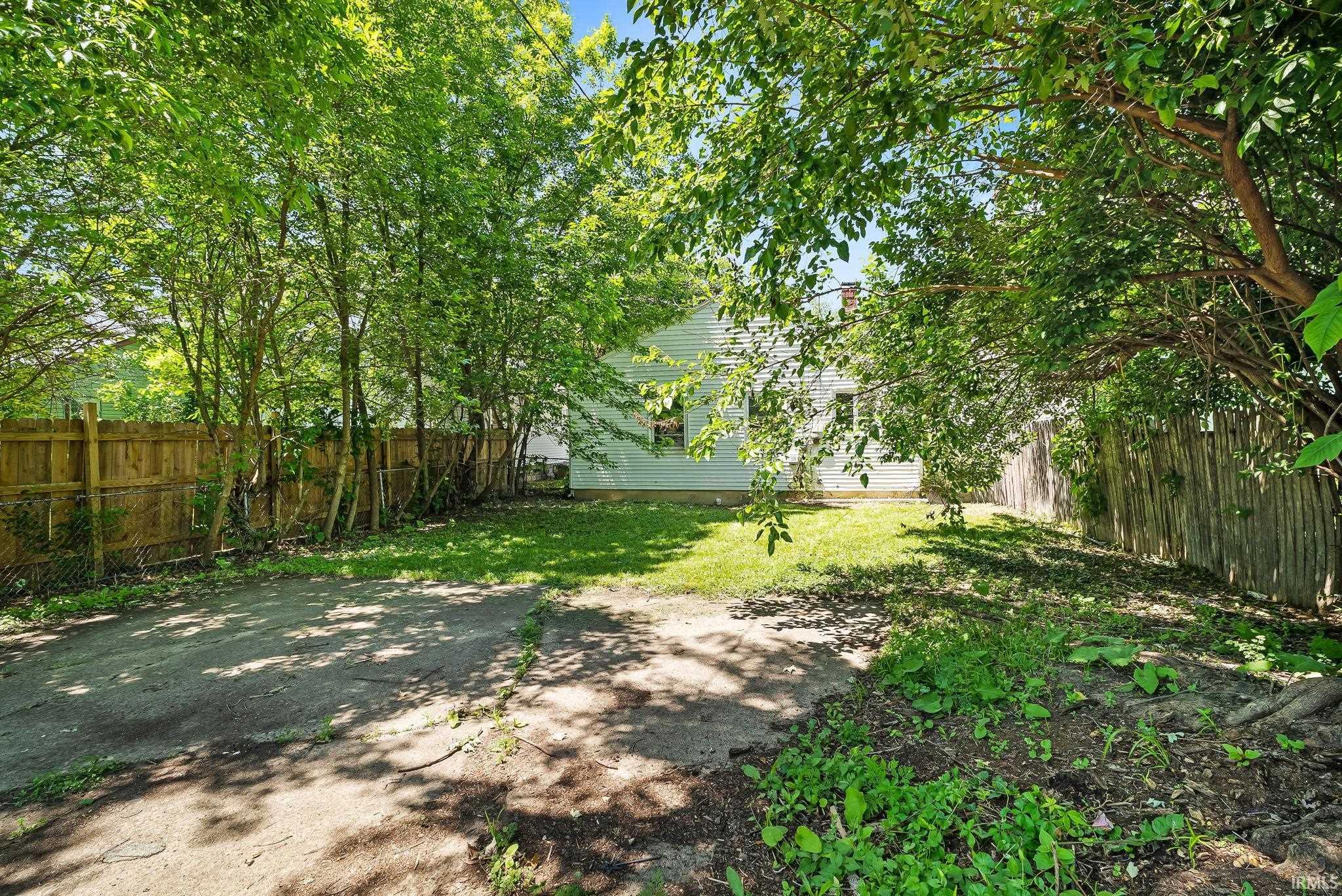 Expansive rear yard featuring green lawn, mature trees, and privacy fencing