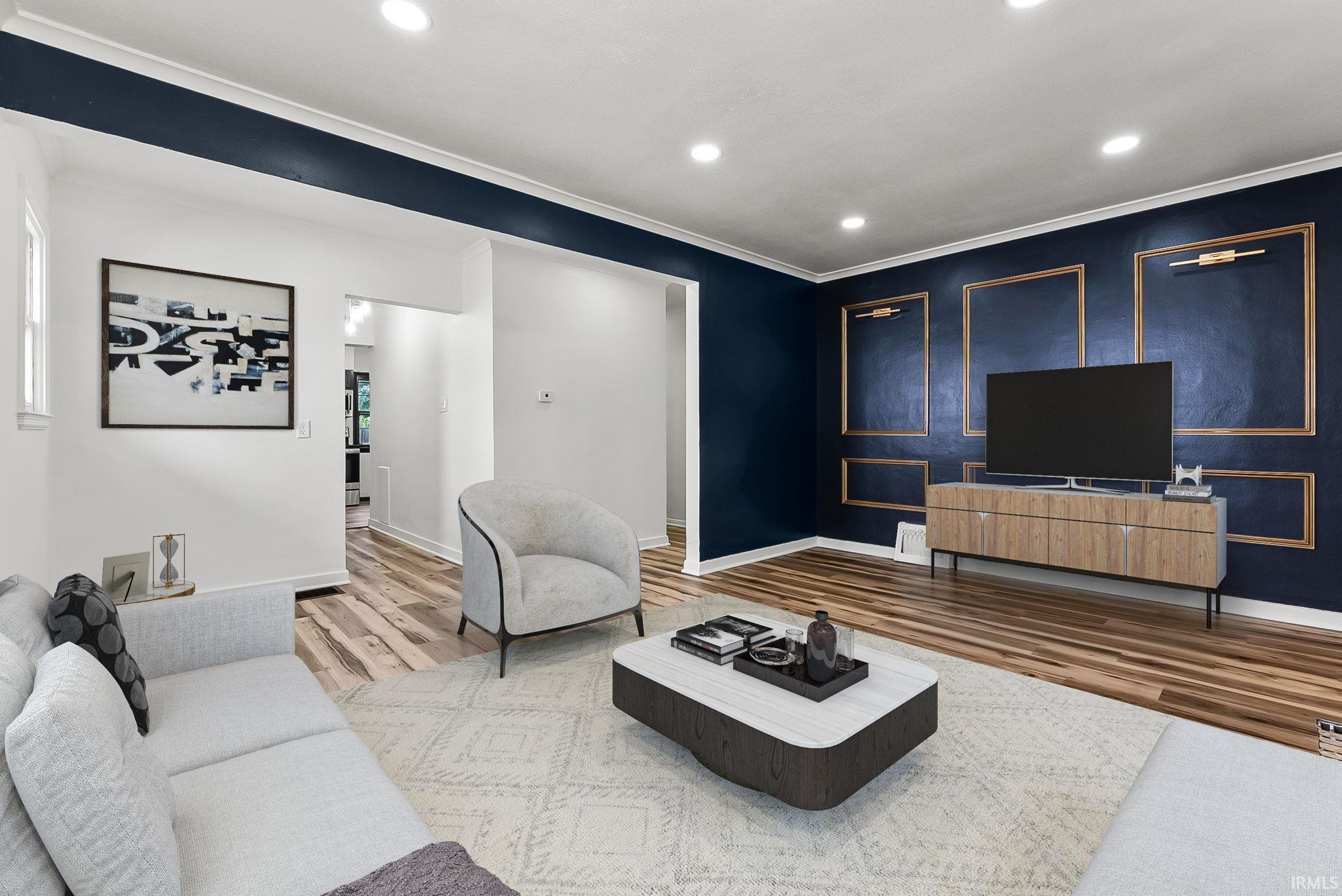 Living space featuring wood-finish flooring, recessed lighting, and a dark accent wall with decorative molding and wall-mounted sconces