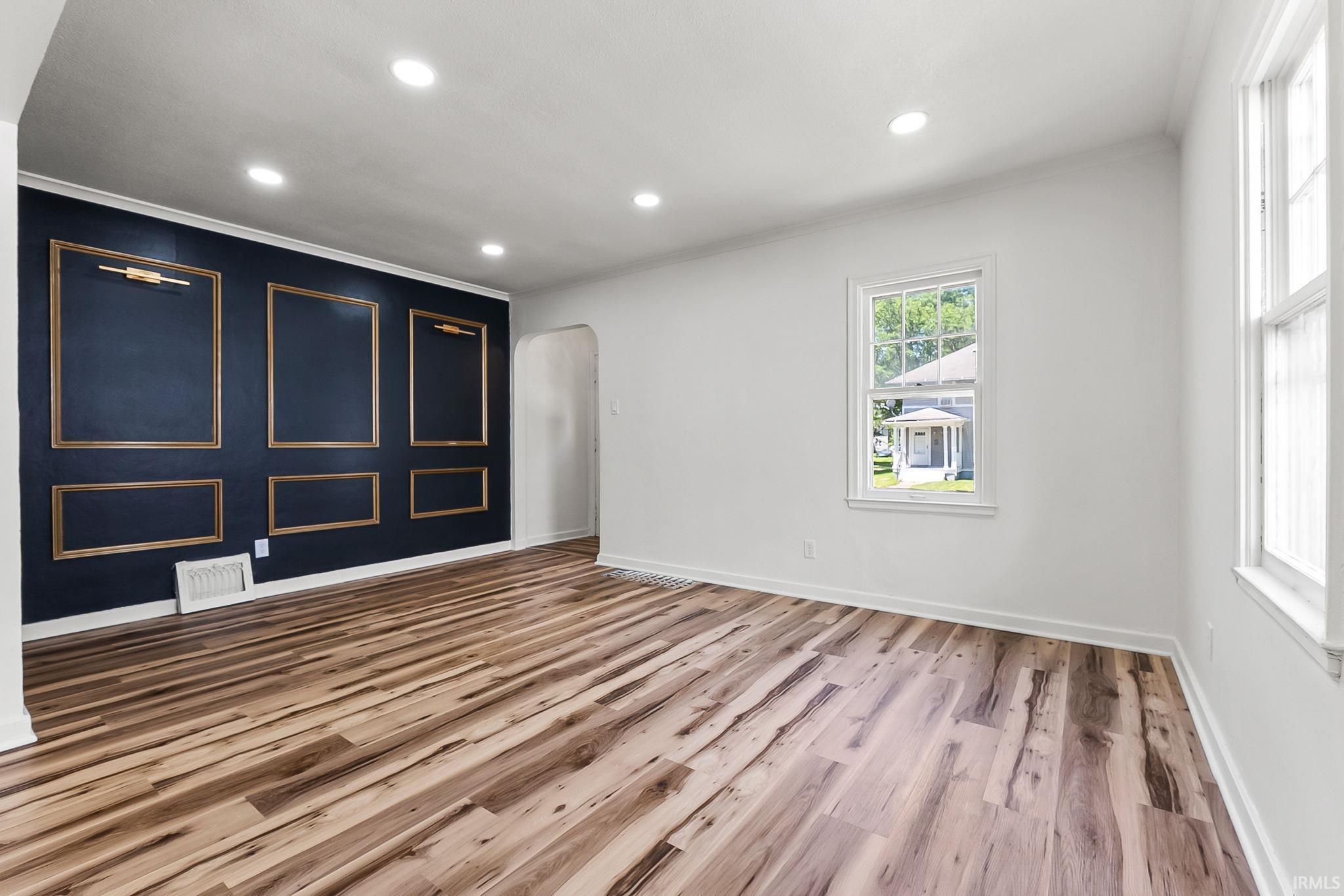 Open-concept living space featuring wood-finish flooring, recessed lighting, and a dark accent wall with decorative molding and sconce lighting