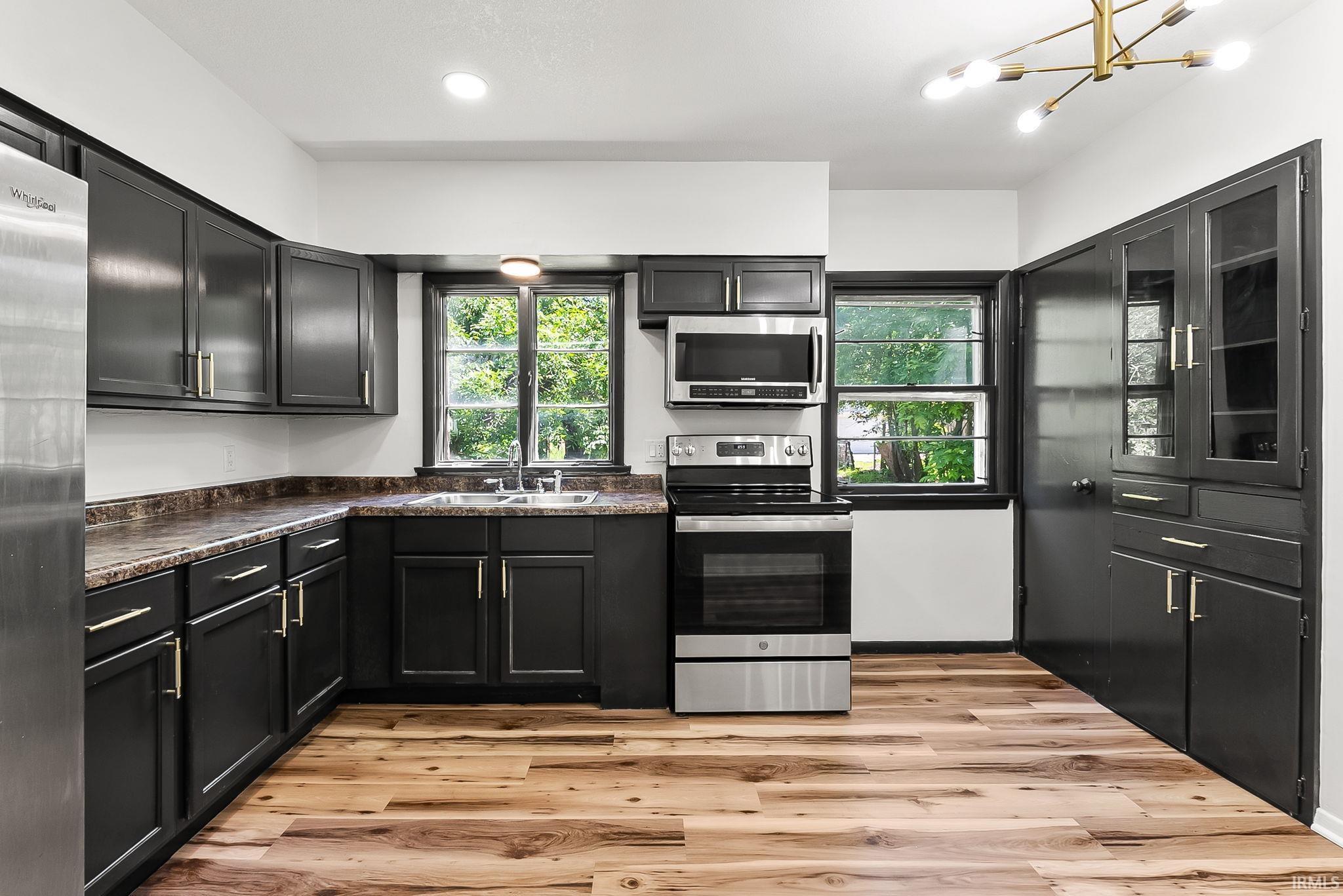 Kitchen featuring dark cabinetry with gold-finish hardware, wood-finish flooring, stainless steel appliances, and a double basin sink