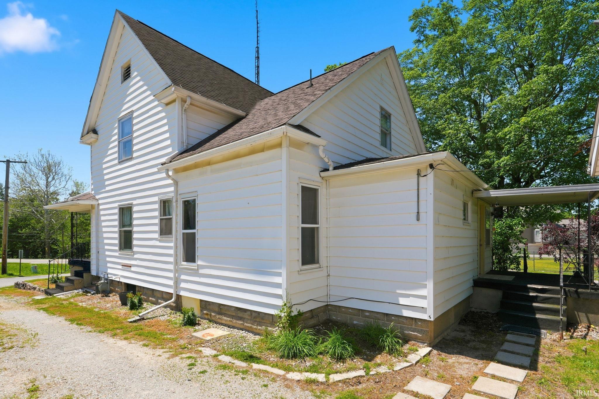 White siding exterior with a dark shingle roof, featuring multiple windows, a covered entrance, and a side porch with a protective awning
