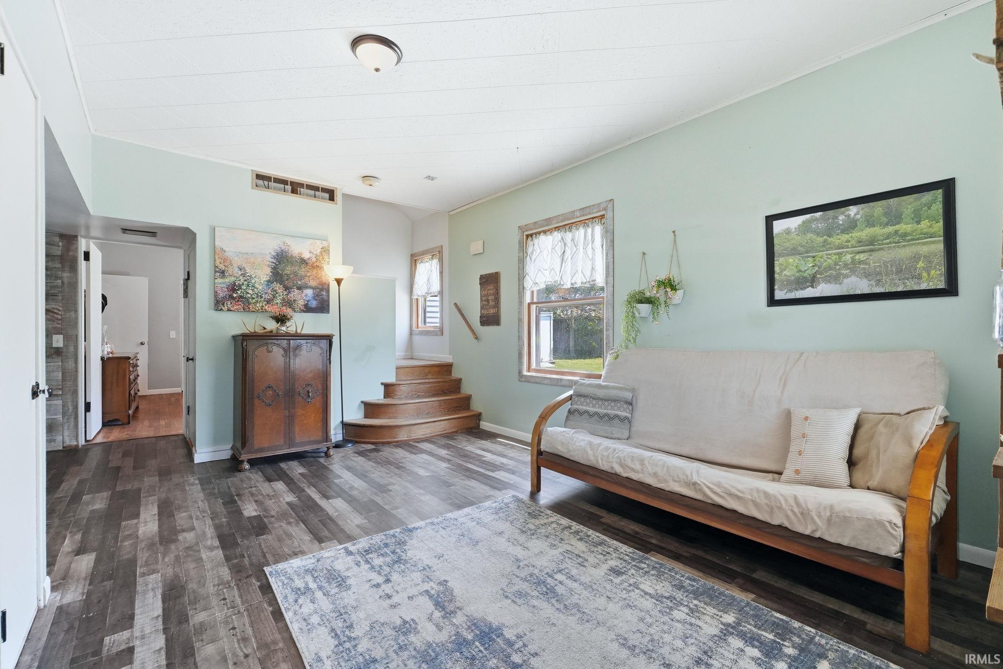 Spacious interior featuring wood-finish flooring, light-toned walls, a window with exterior visibility, a built-in staircase, and an overhead light fixture