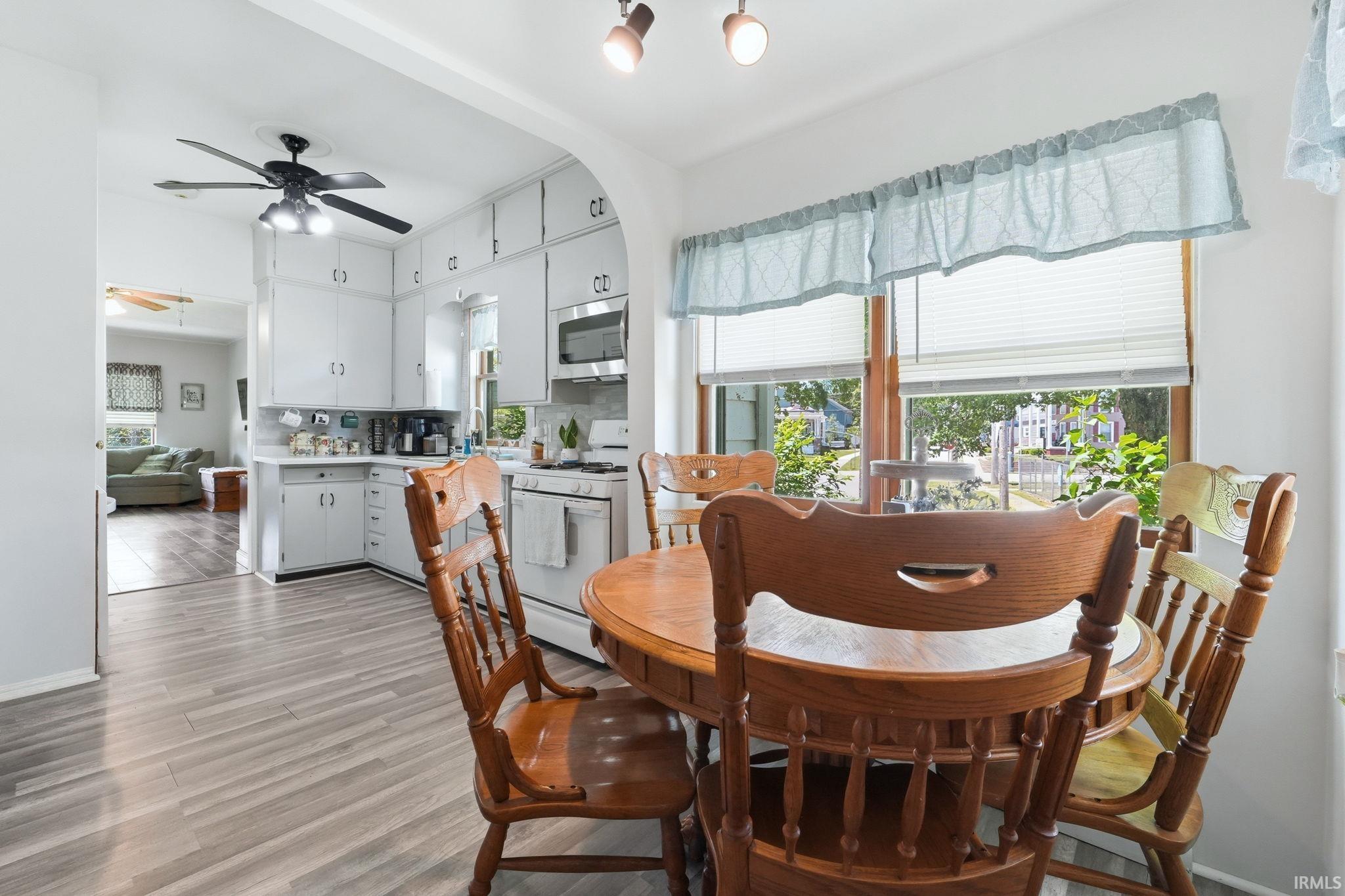 Bright dining area featuring wood-finish flooring, a window with pleated blinds, an arched entryway, and recessed ceiling lighting