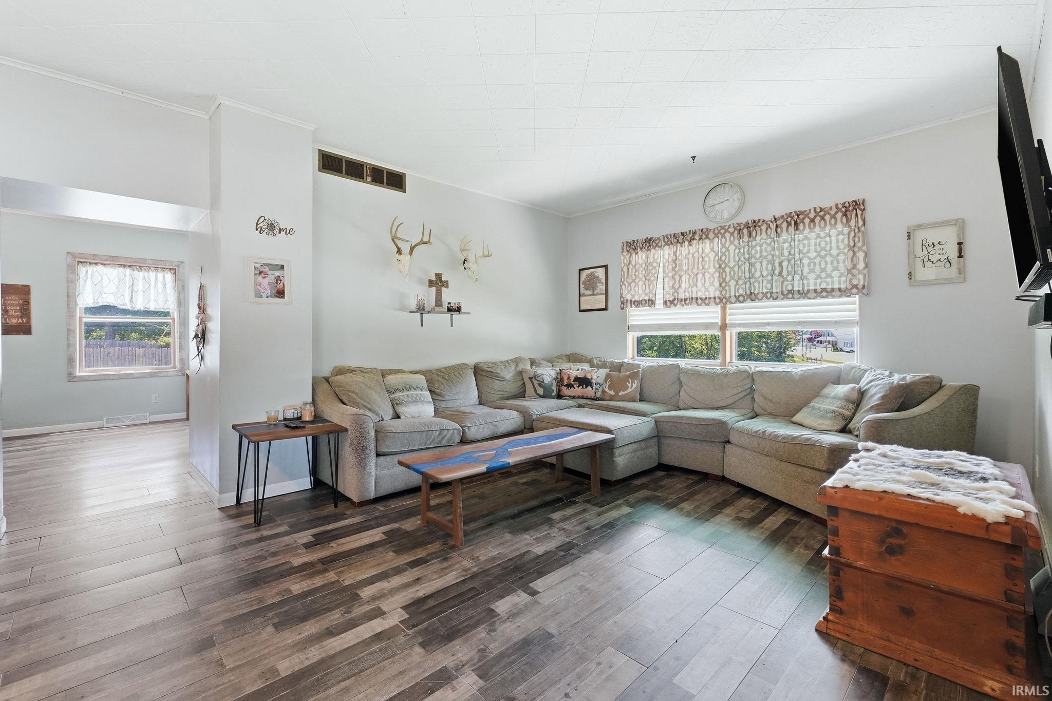 Spacious living area featuring wood-finish flooring, a neutral color palette, and ample natural light from multiple windows