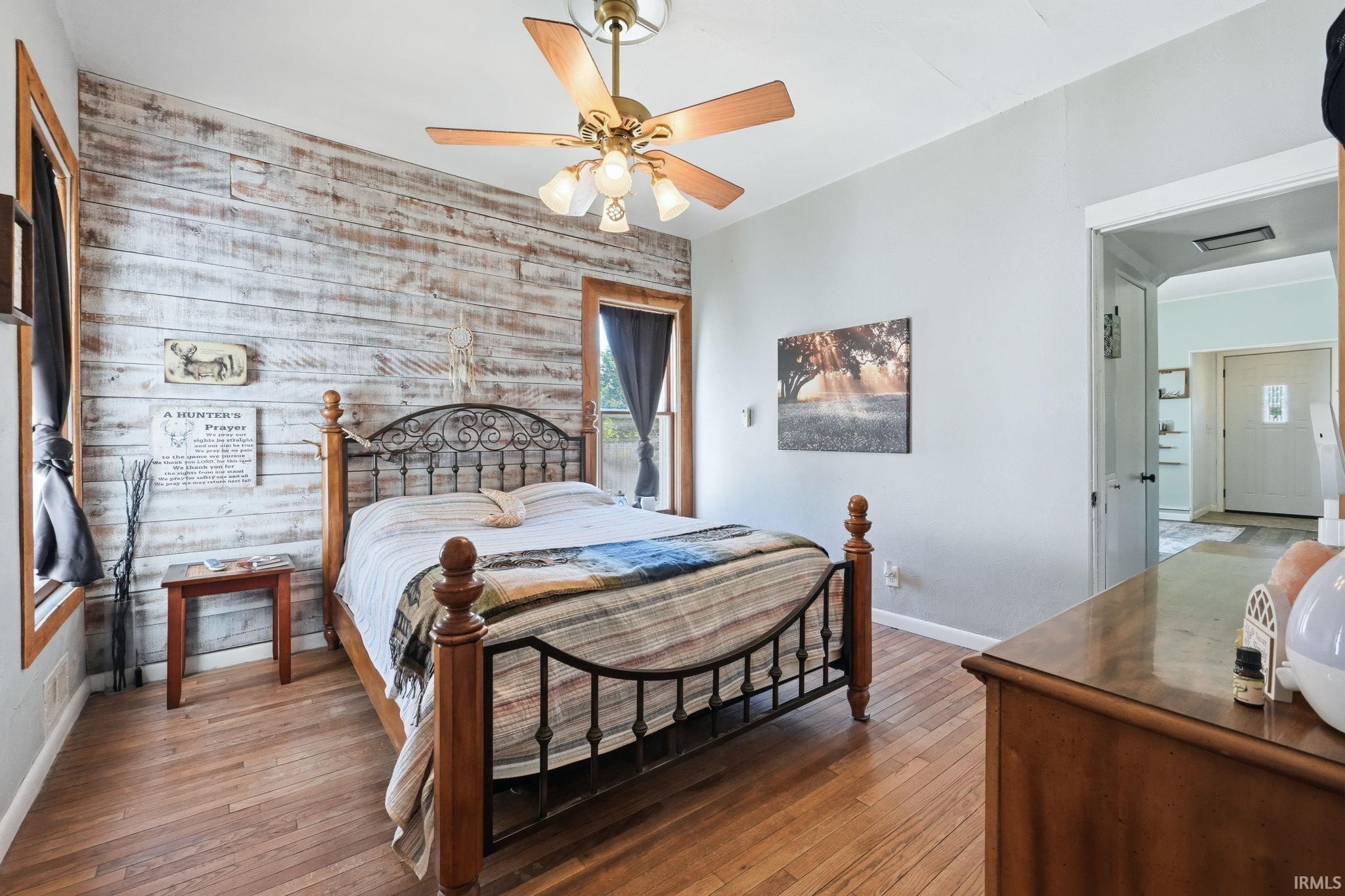 Bedroom featuring a shiplap accent wall, wood-finish flooring, and a ceiling fan with integrated lighting