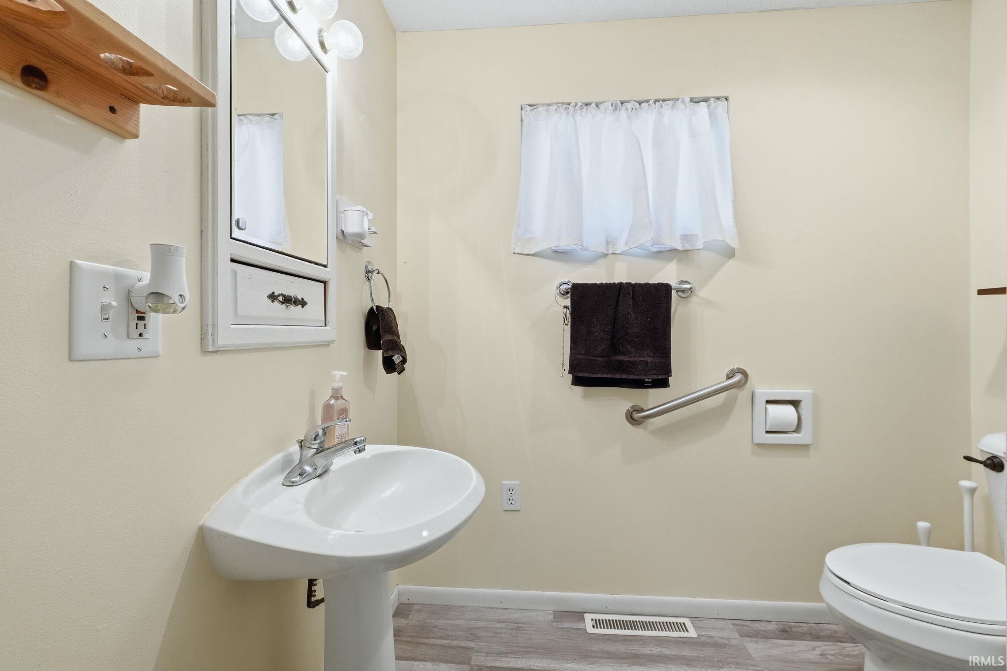 Pedestal sink with chrome faucet, framed mirror with integrated lighting, wood-finish flooring, and light-toned wall paint