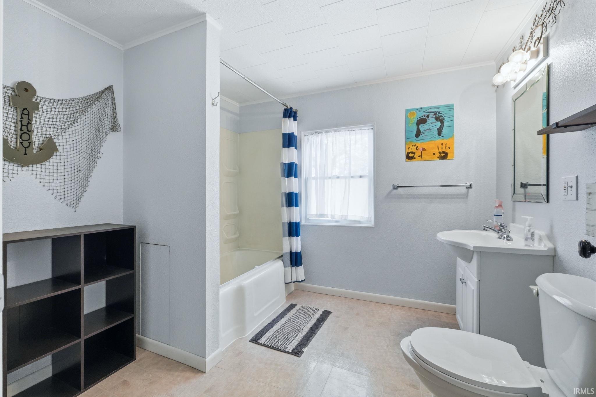 Bathroom featuring a white vanity with a single sink, an integrated tub and shower combination, and a window with white sheers
