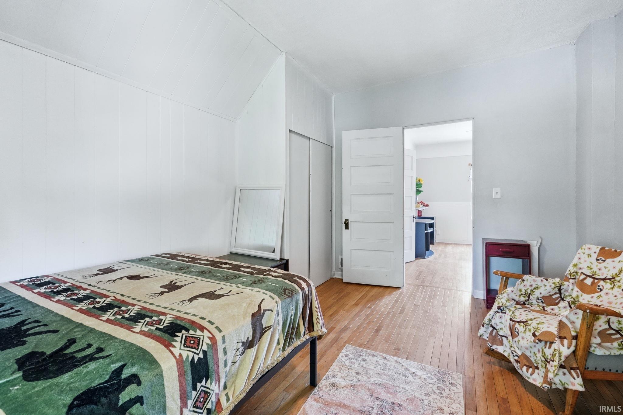 Bedroom featuring wood-finish flooring, white paneling walls, and an angled ceiling