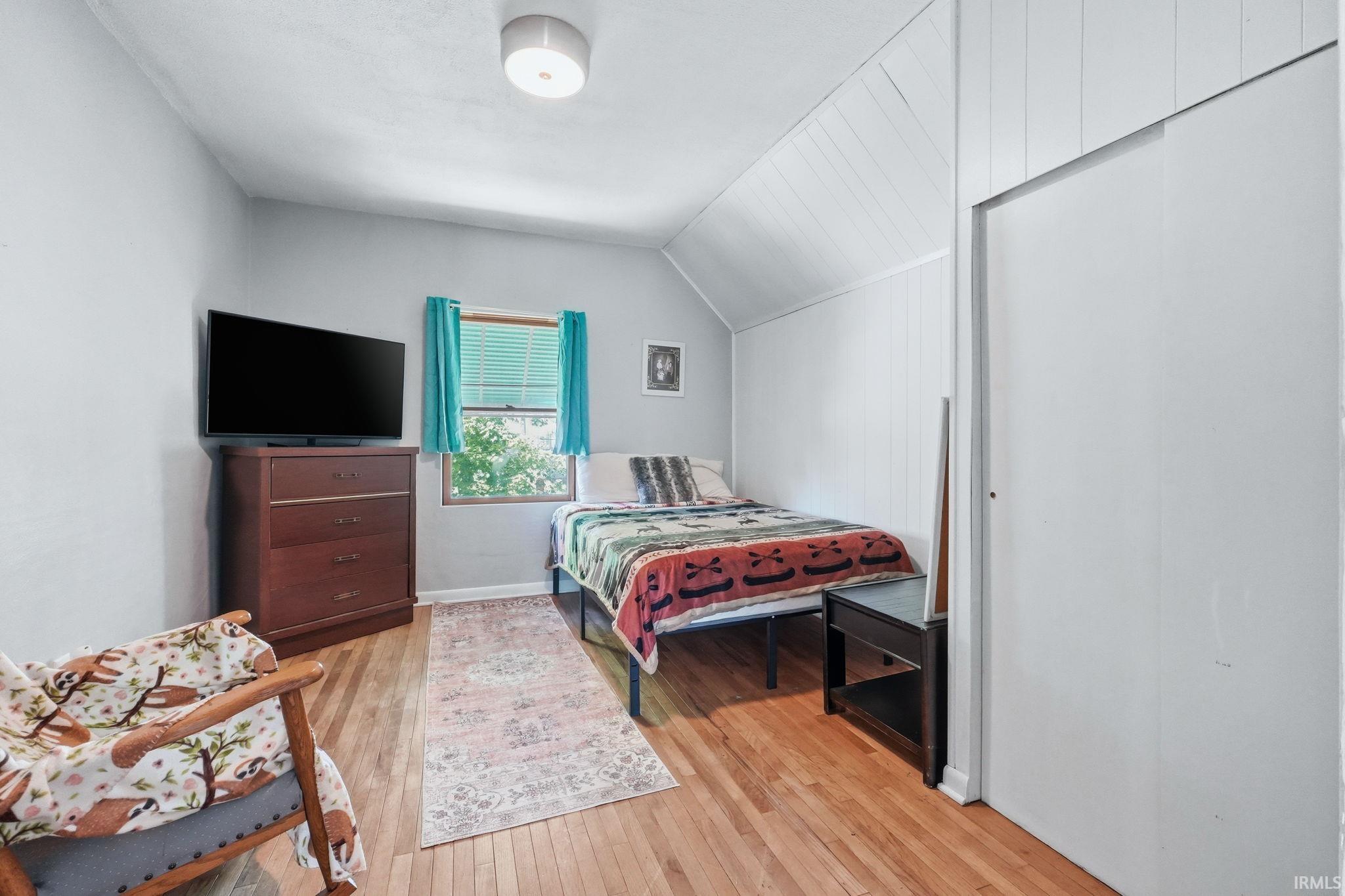 Hardwood flooring throughout, featuring a window with blinds, and white paneled walls