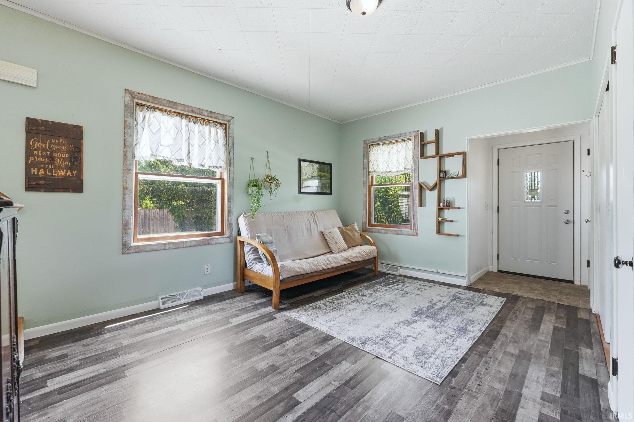 Living area featuring wood-finish flooring, two large windows with distressed wood frames, and a white paneled entry door with frosted glass insert