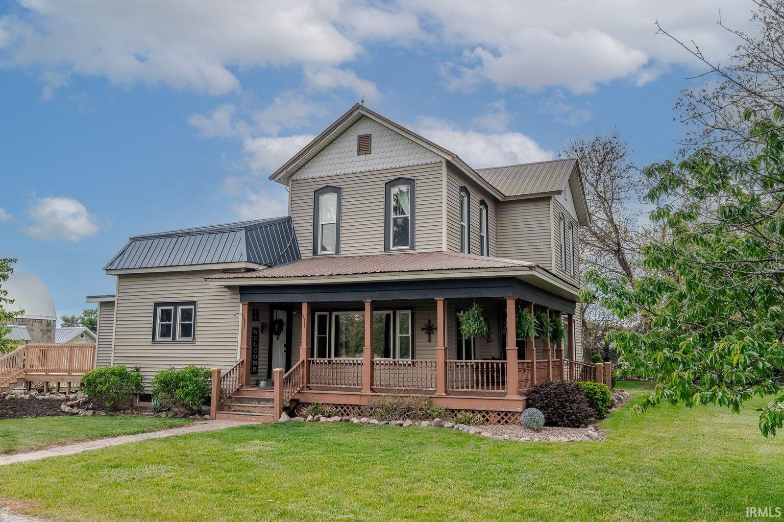 Two-story residence featuring light gray siding with contrasting dark trim, a full-width covered porch with wood railings, and a dark metal roof