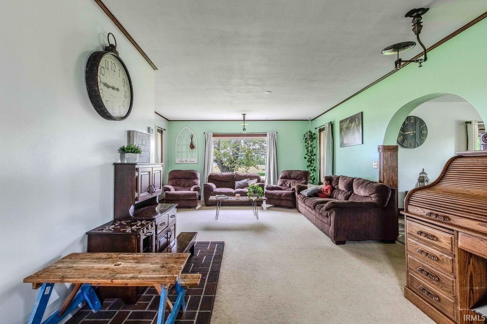 Spacious living area featuring light-colored carpet, a large window with outdoor visibility, and an arched entryway