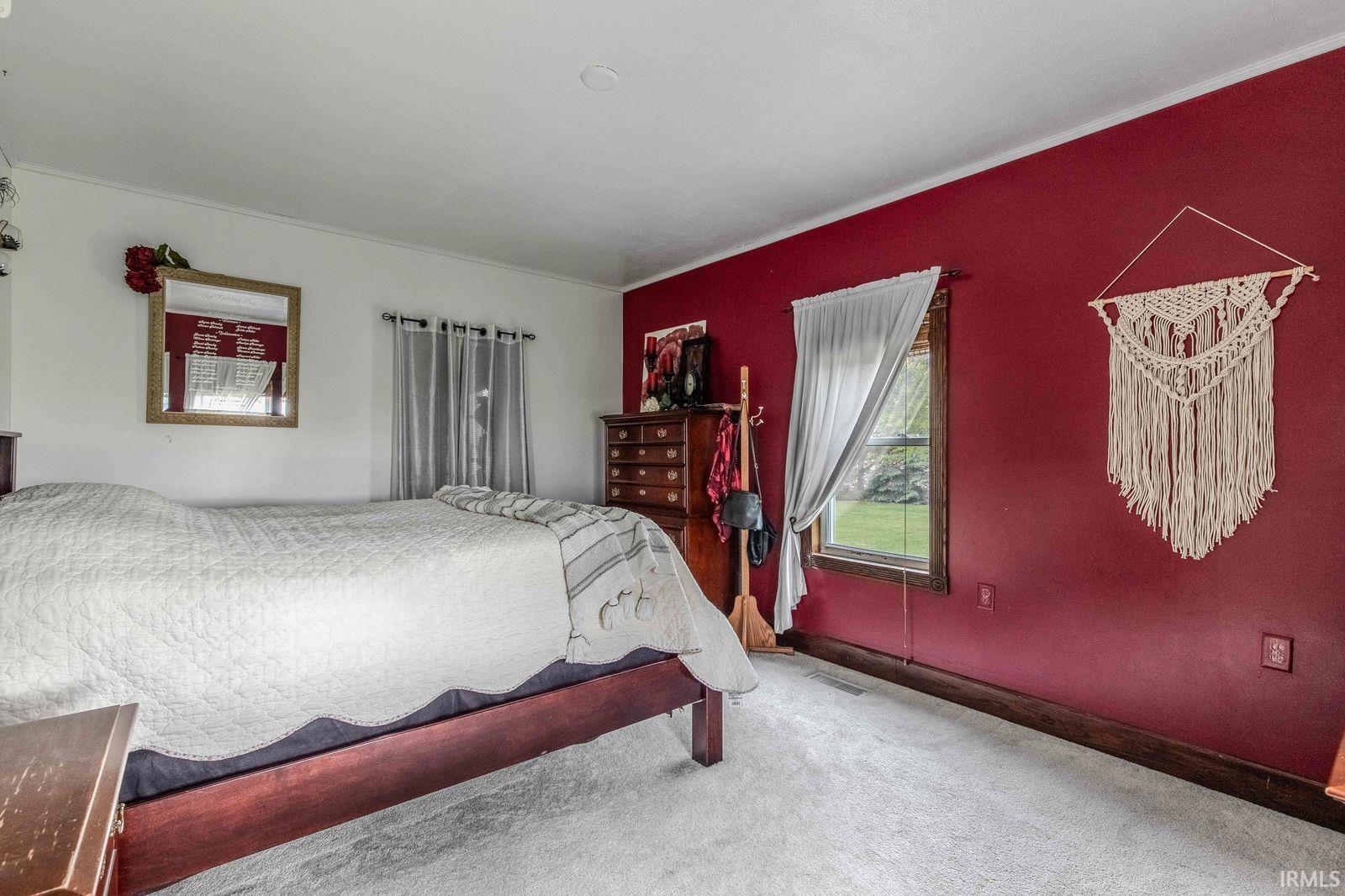 Bedroom featuring a window with natural light, a contrasting accent wall, and light-colored carpeting