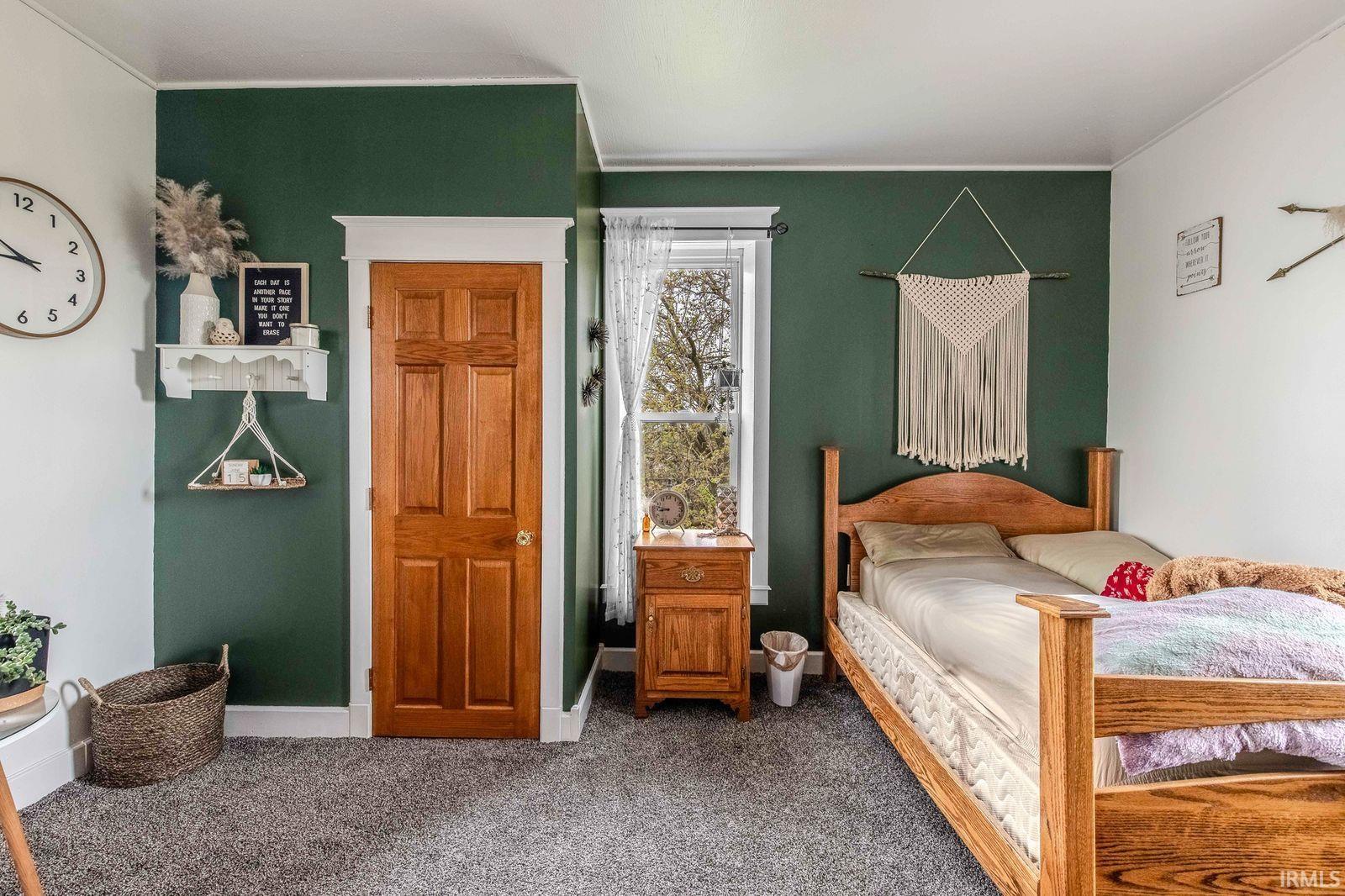 Bedroom featuring textured gray carpeting, a window with natural light, and a paneled wooden door
