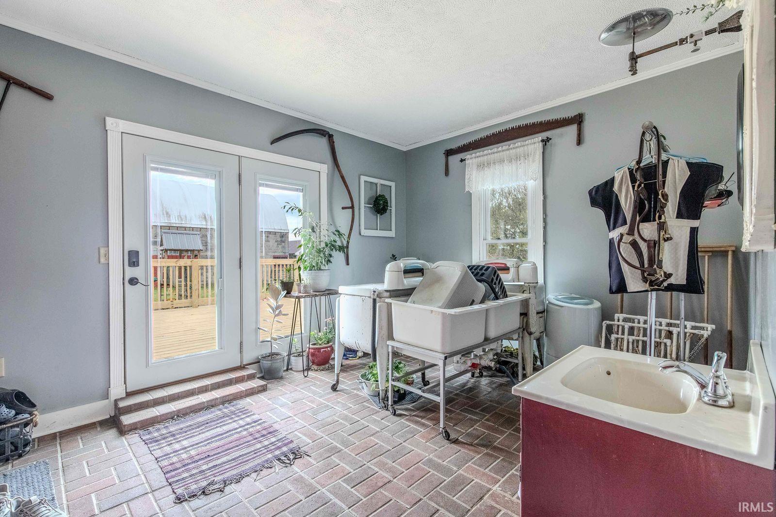 Brick paver flooring throughout this versatile utility room featuring double glass-paneled doors, a red wood-finish vanity with an integrated sink, and an additional window providing natural illumination