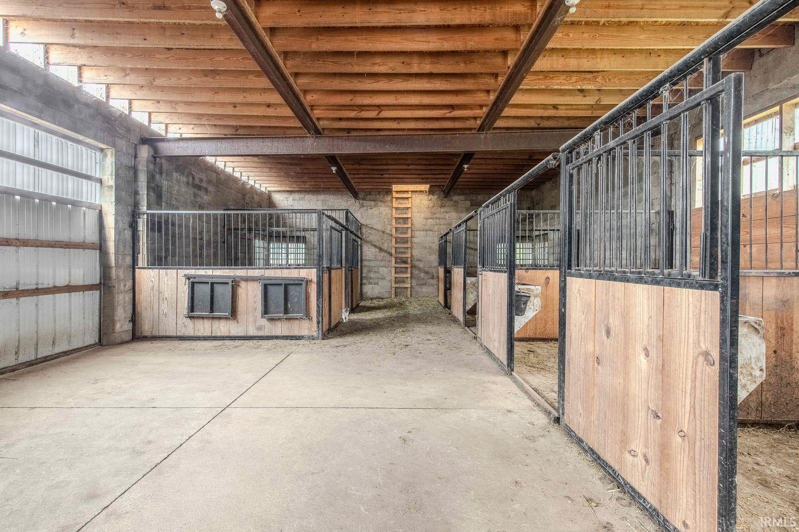 Spacious barn interior featuring multiple stalls with wood paneling and metal gating