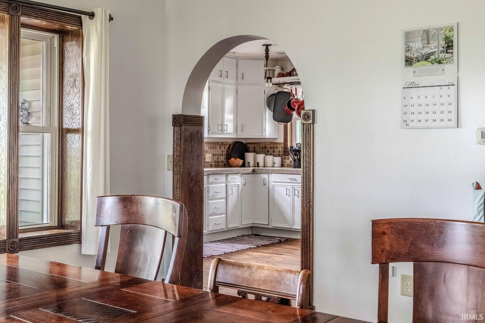 Archway entry to the kitchen, featuring white cabinetry and a mosaic tile backsplash