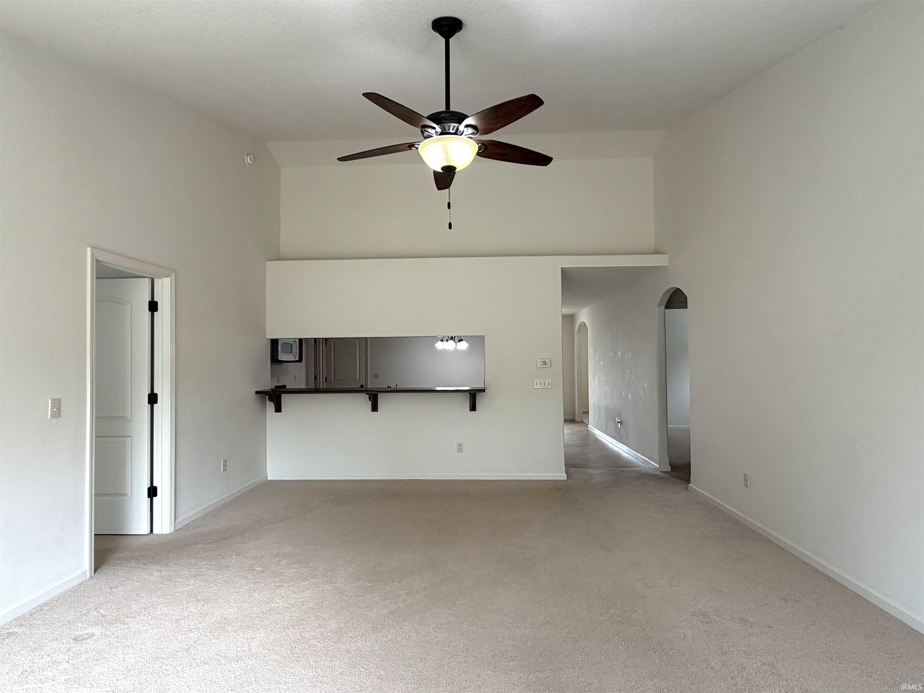 Vaulted ceilings with a ceiling fan, pass-through window with bar seating, arched doorways, and carpeted flooring