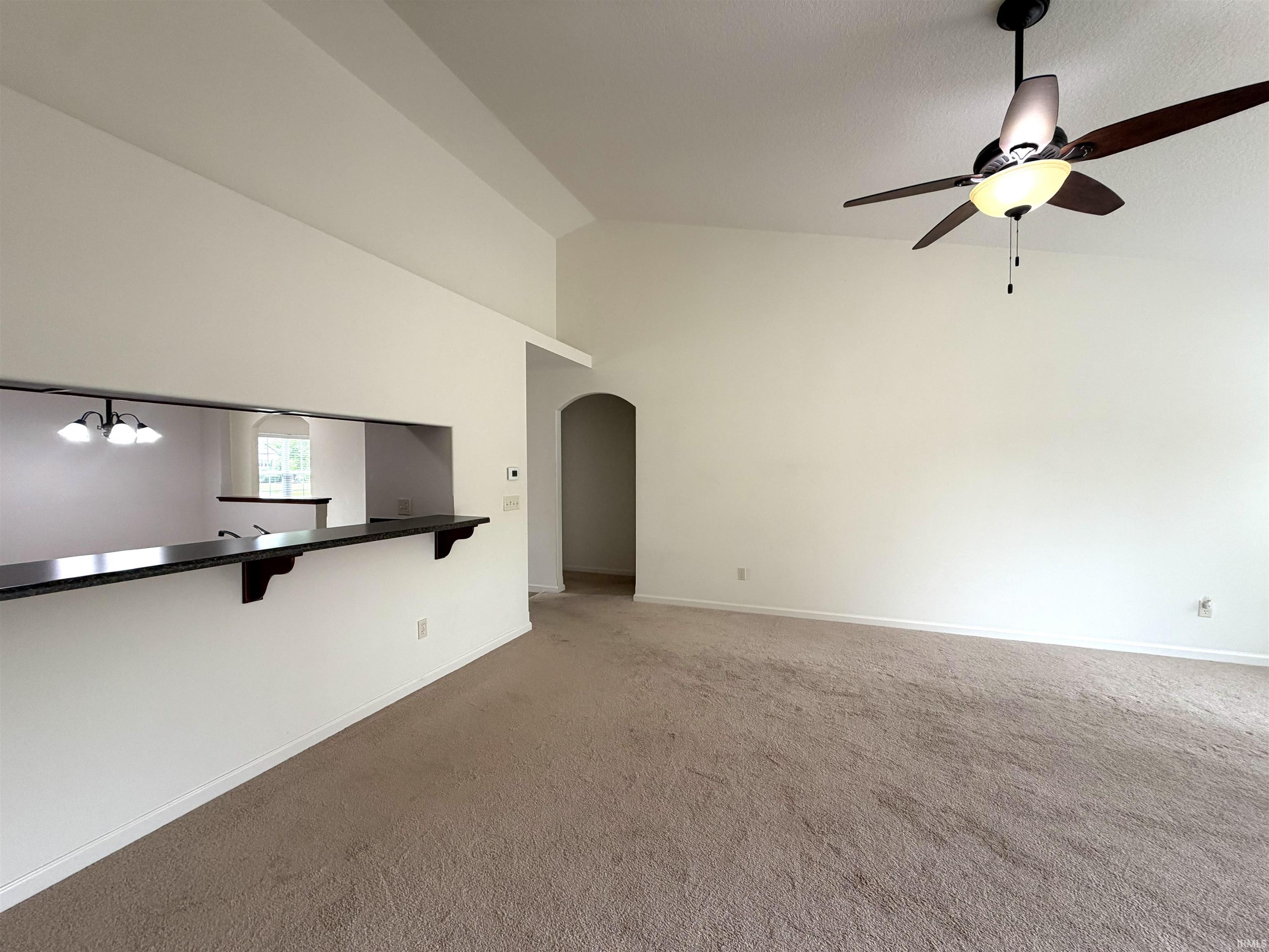Living area featuring vaulted ceilings, a ceiling fan with integrated lighting, and carpet flooring