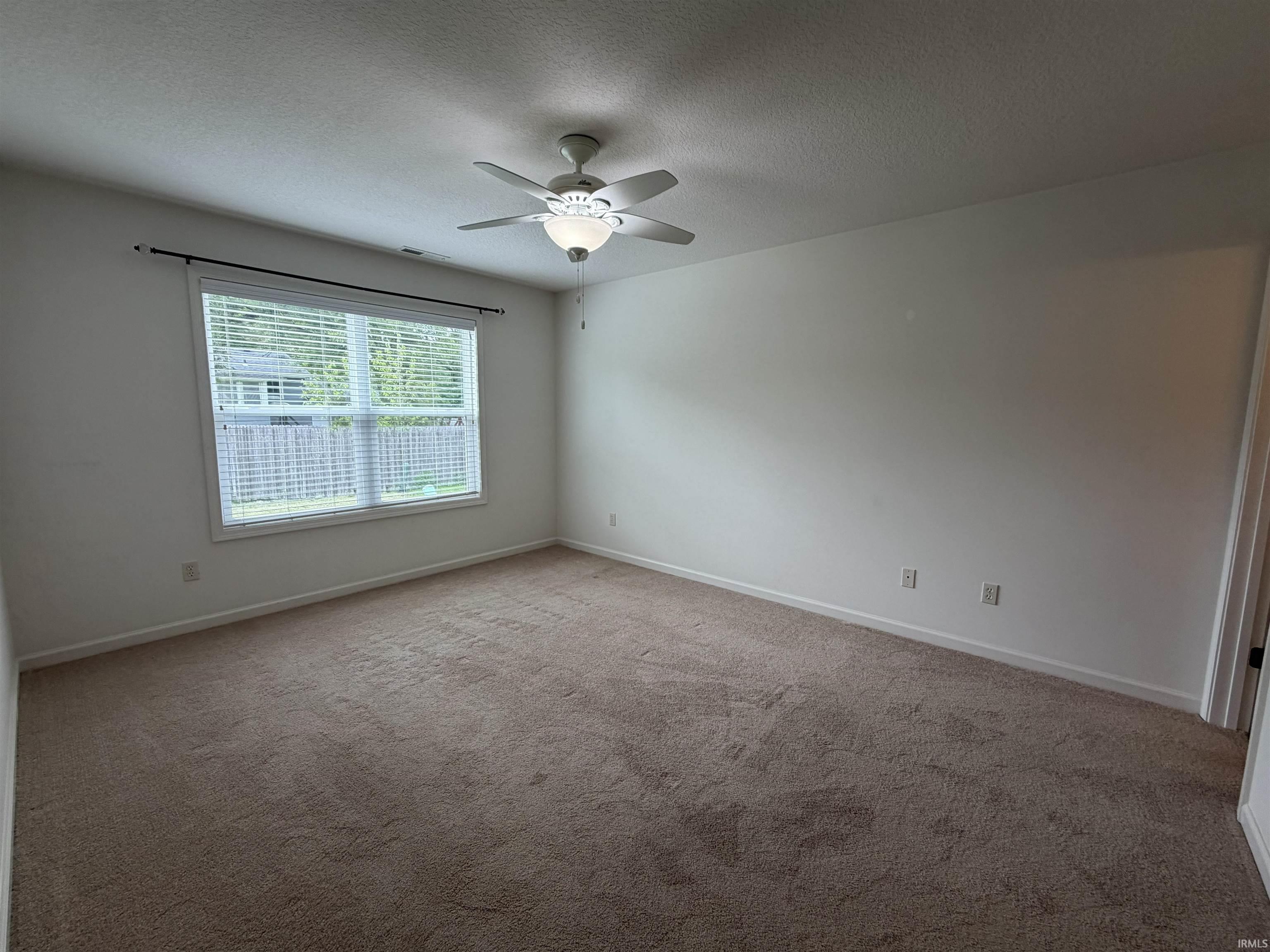 Spacious room featuring neutral carpeting, a large window with blinds, and a ceiling fan with integrated lighting