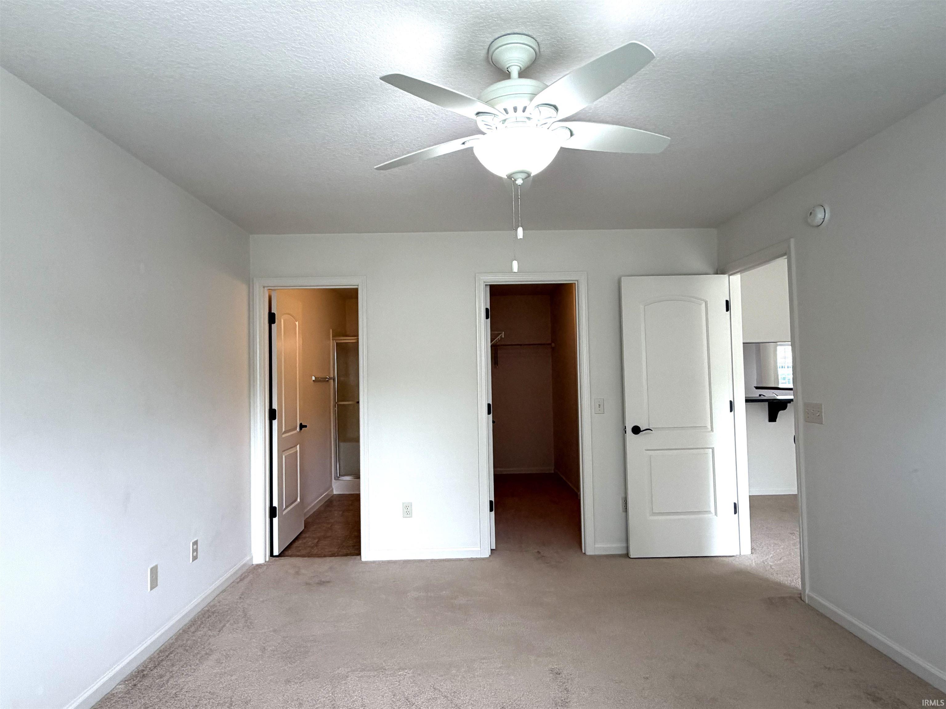 Neutral tone carpet flooring with white walls and a ceiling fan with integrated lighting