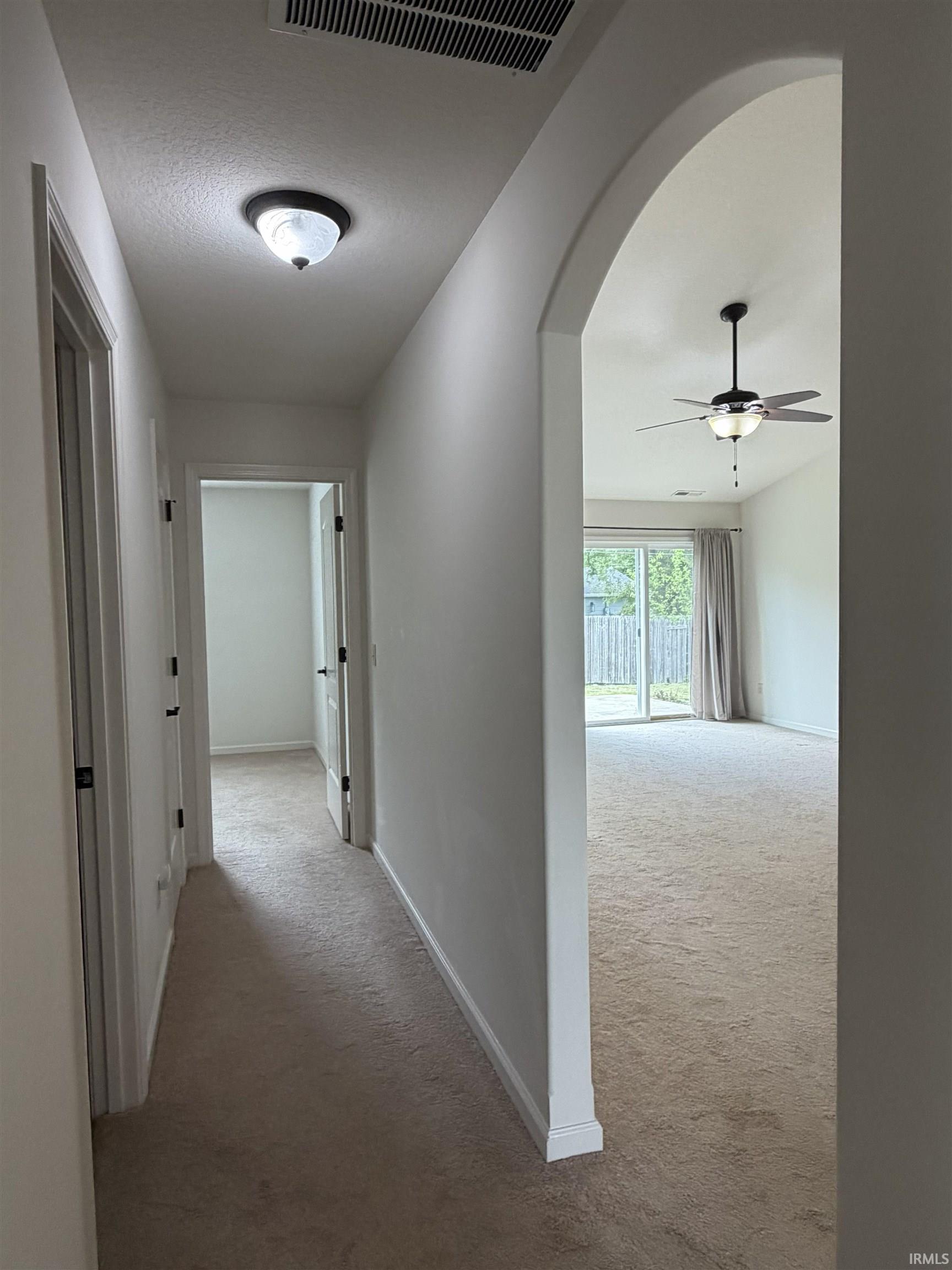 Hallway featuring neutral carpet, white walls, and an arched entry to a living space with a ceiling fan and sliding glass doors