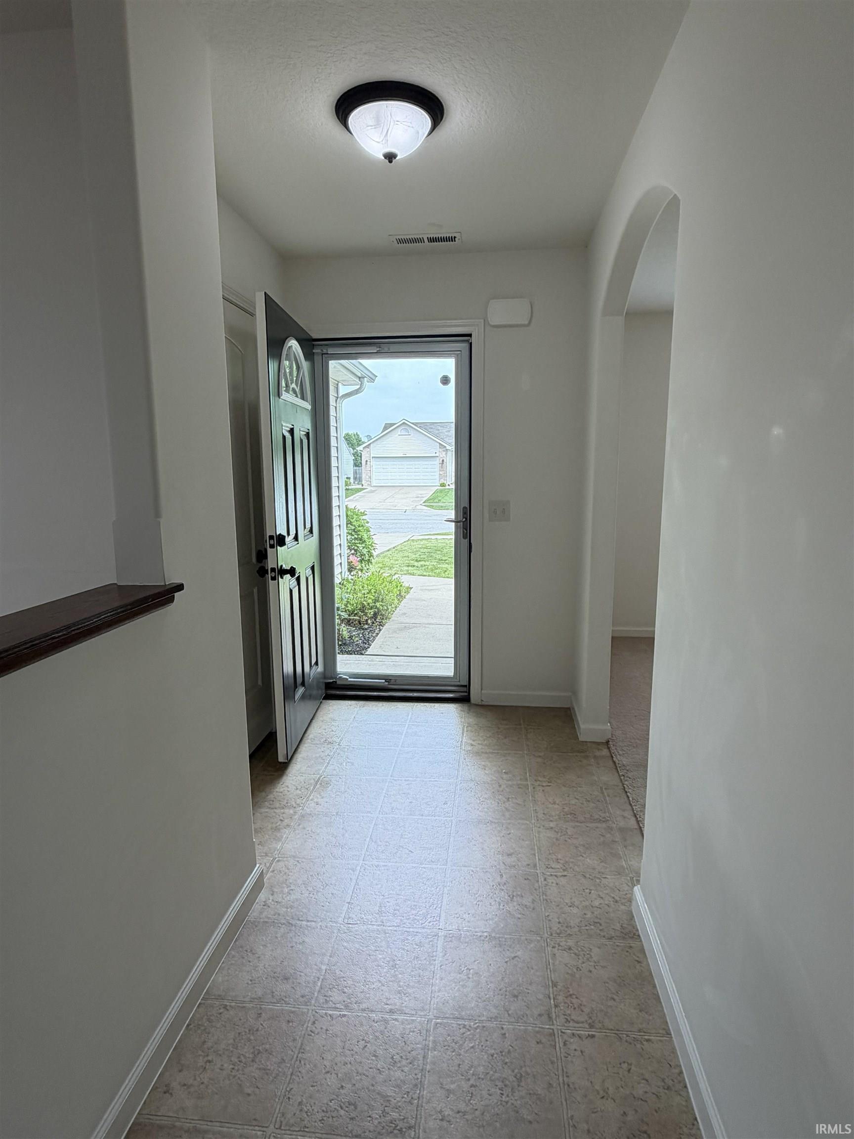 Welcoming entryway featuring tiled flooring, a decorative archway, a half-wall with wood trim, and a semi-flush mount ceiling fixture