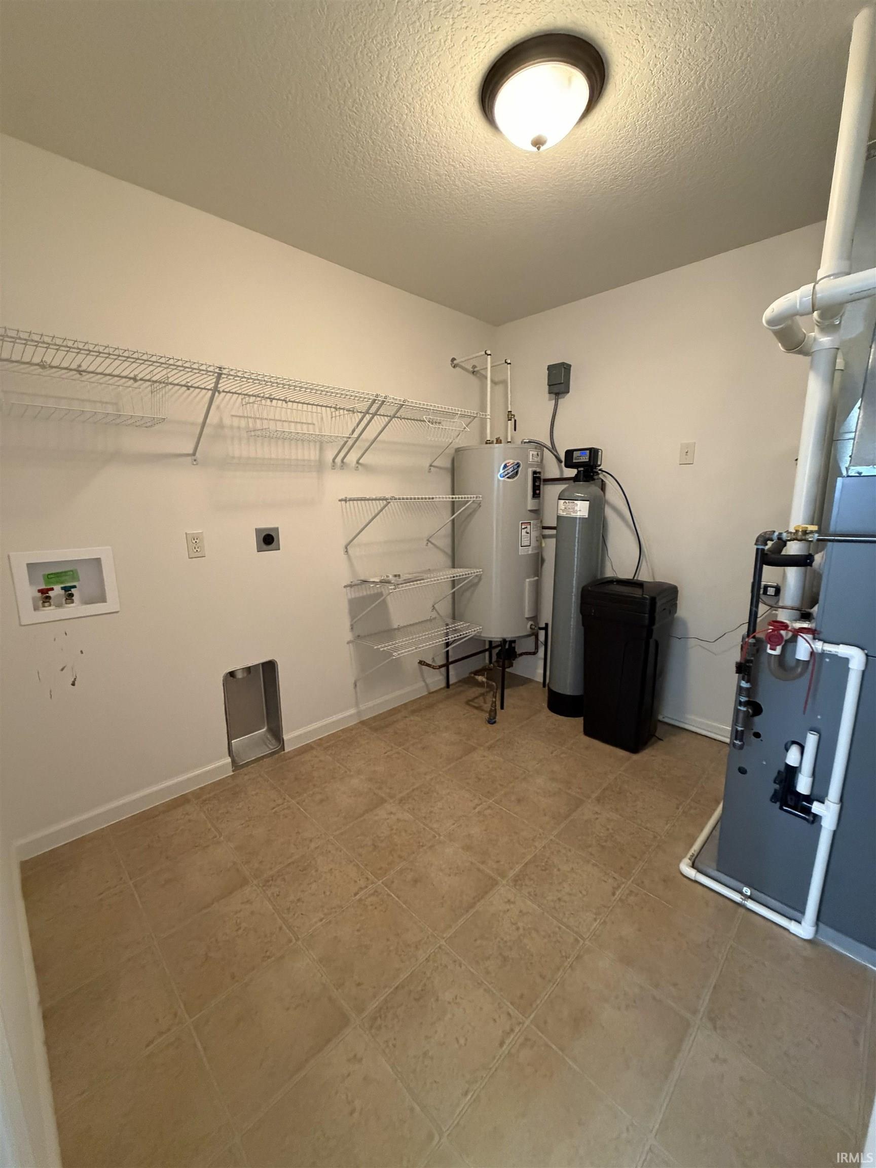 Utility room featuring tile flooring, built-in wire shelving, and overhead lighting