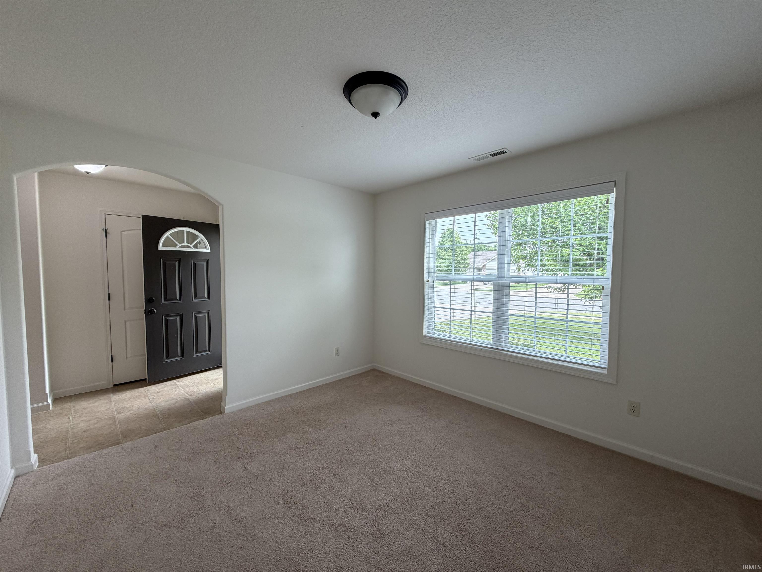 Carpeted living space featuring an arched doorway and a large window with blinds