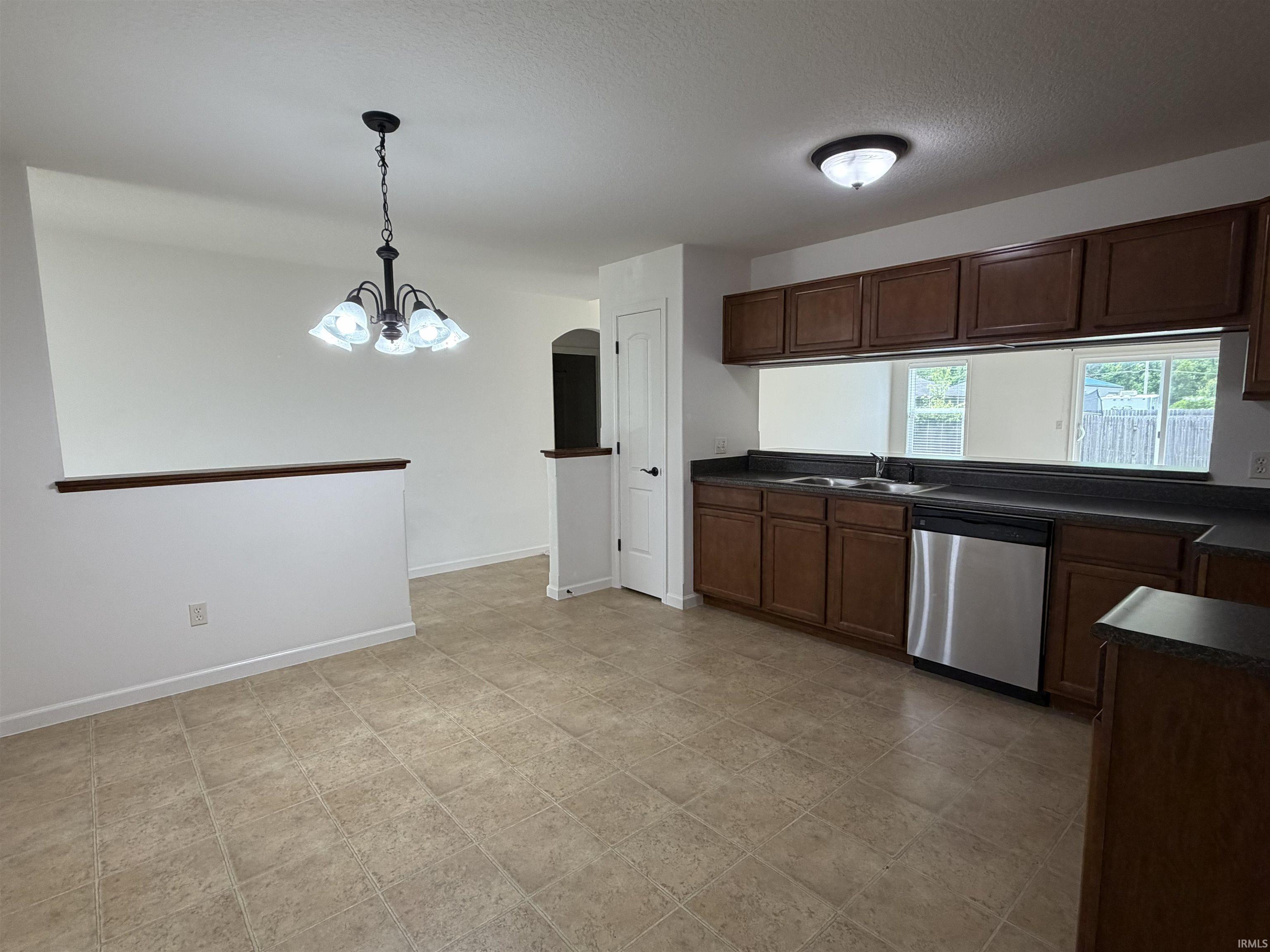 Kitchen and dining area featuring a tile floor, dark wood-finish cabinetry, stainless steel dishwasher, and a contemporary chandelier